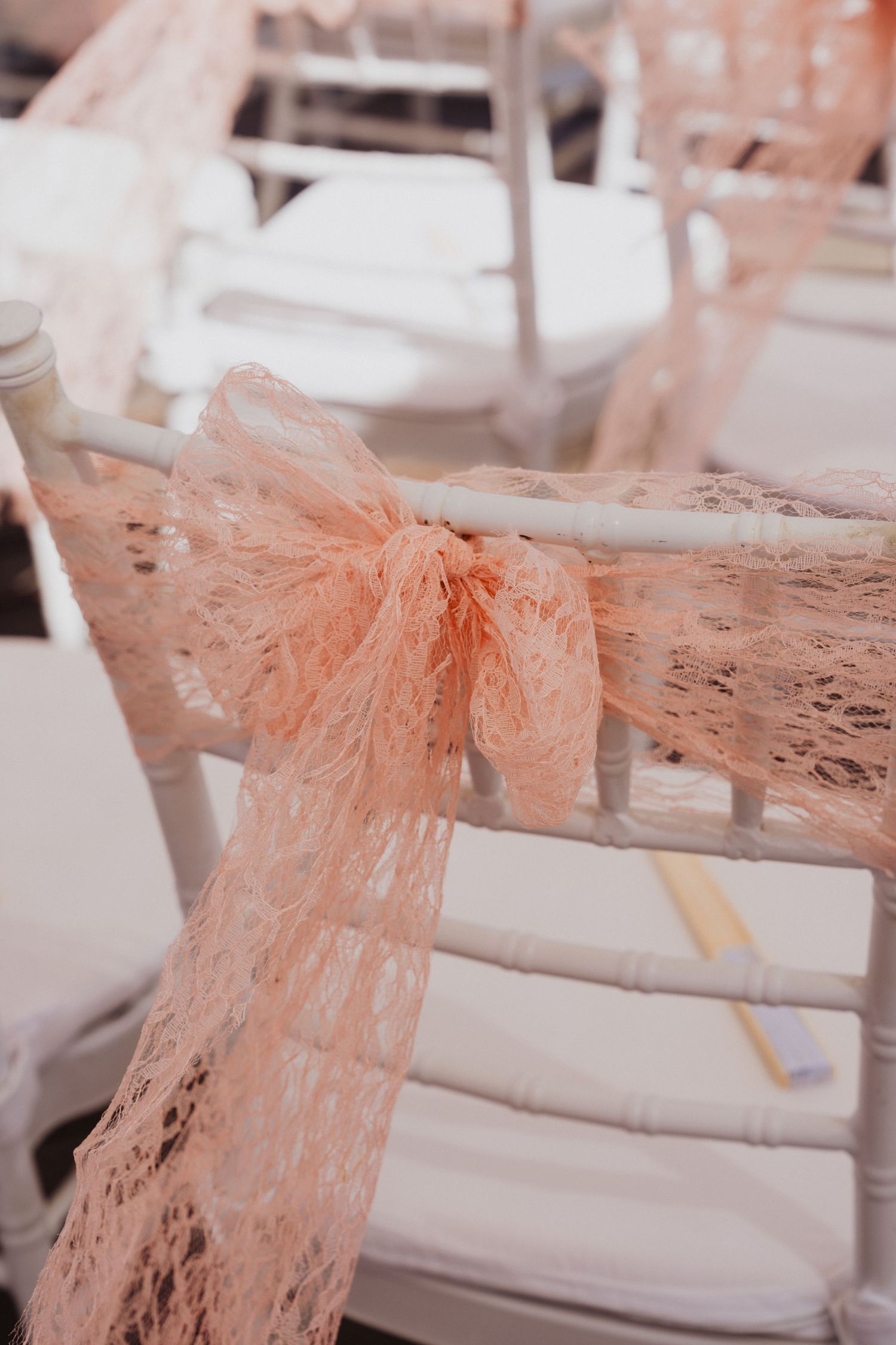 Delicate peach lace bow detail on white wedding ceremony chairs.