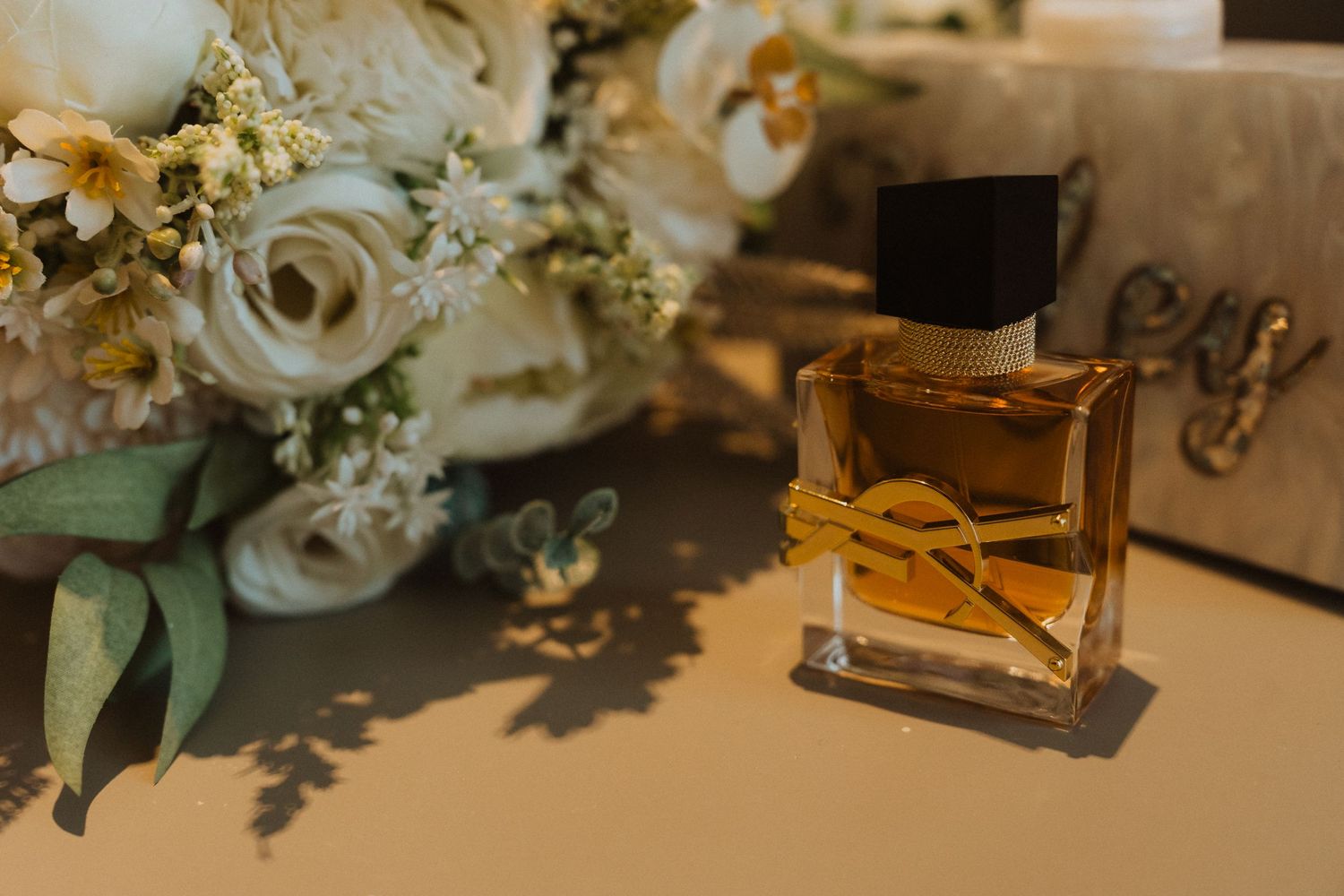 Wedding day details featuring perfume bottle and white rose bouquet in warm light.