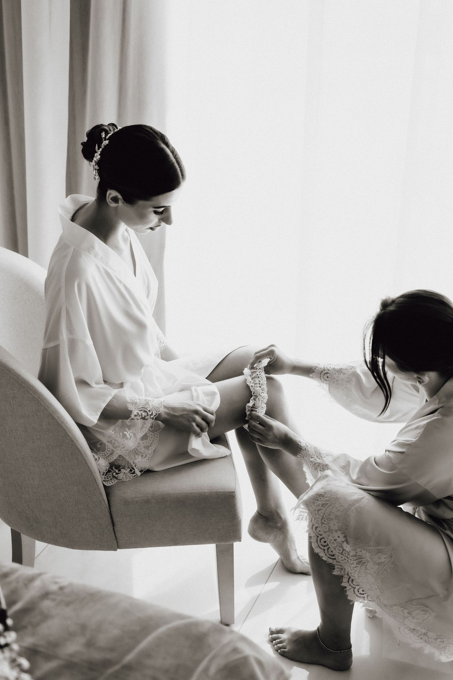 Black and white image shows preparation session with two people in elegant robes.