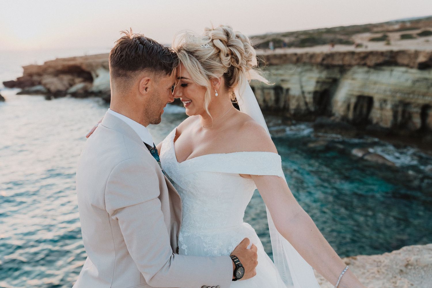 Seaside wedding portrait with turquoise waters and rocky cliffs as backdrop.