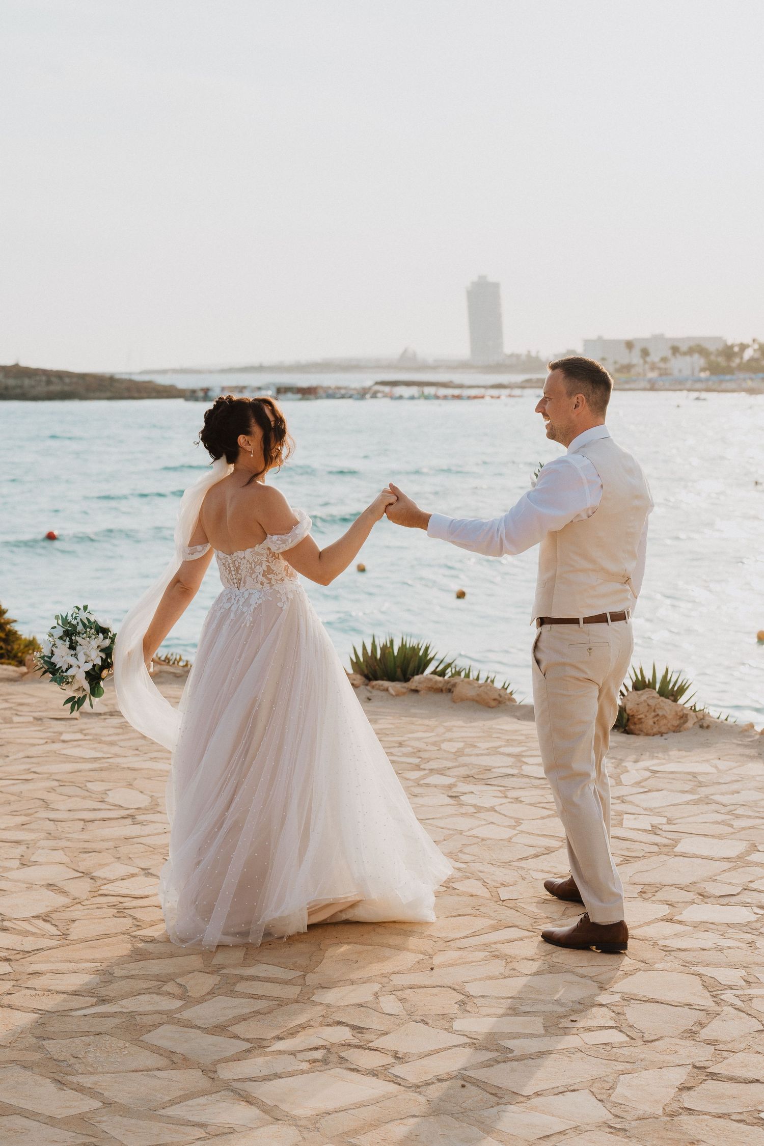 A couple dancing on a seaside terrace during their coastal wedding ceremony at sunset.