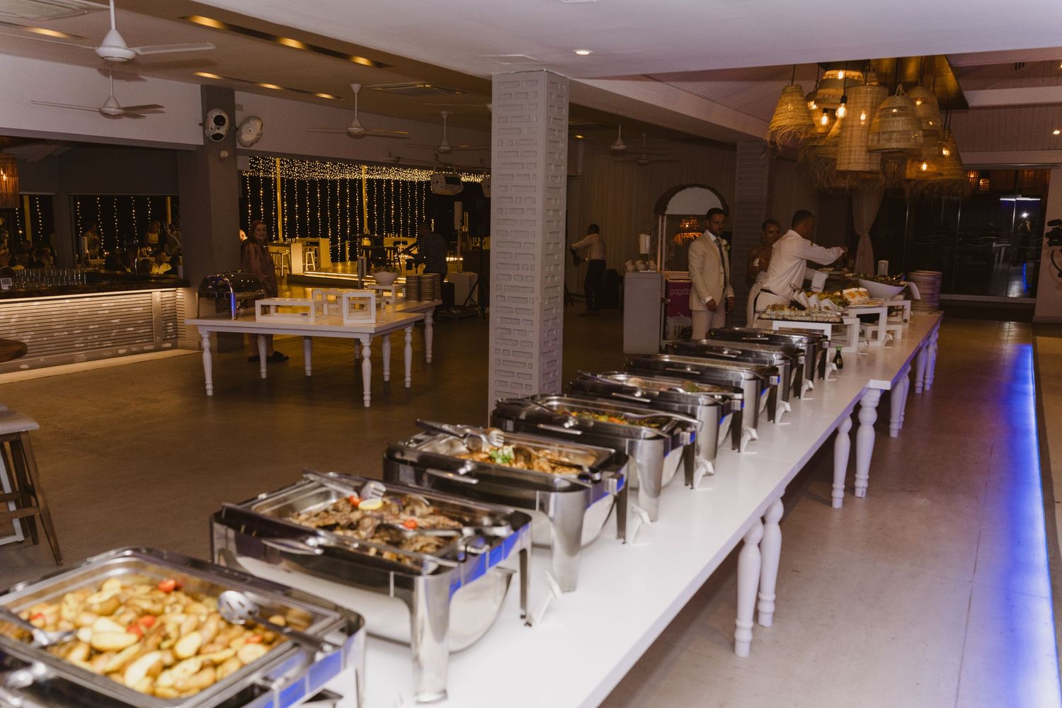 Long buffet table with chafing dishes set up in an elegant reception venue.