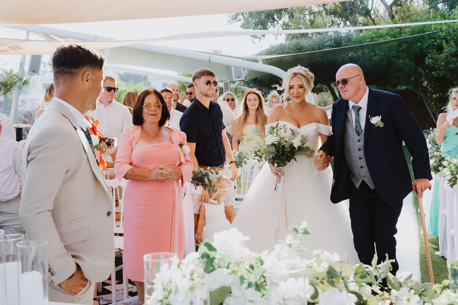 A wedding ceremony taking place outdoors under a canopy with floral arrangements and white decor.