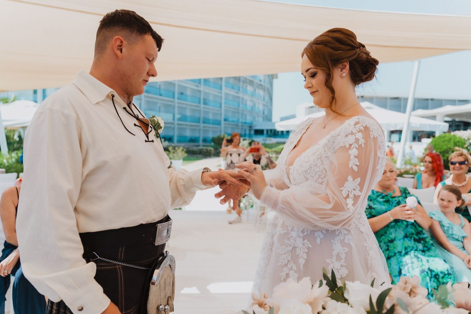 A couple exchanges rings during a romantic beach wedding ceremony under a white canopy with turquoise decor.