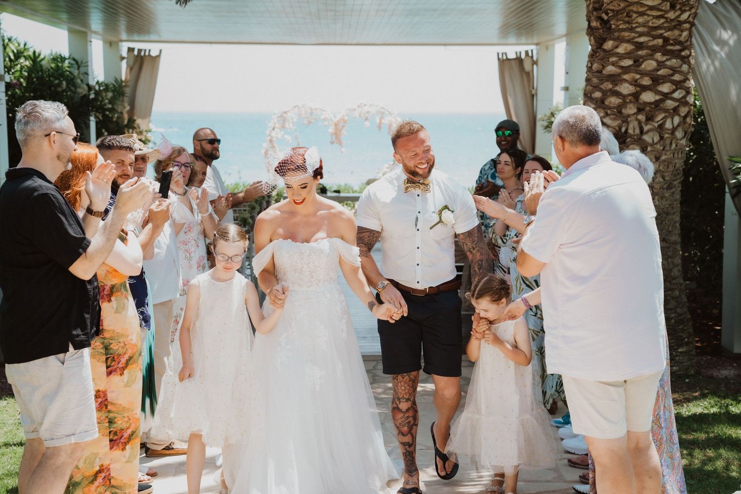 Wedding celebration with guests cheering as the couple walks through an outdoor pathway.