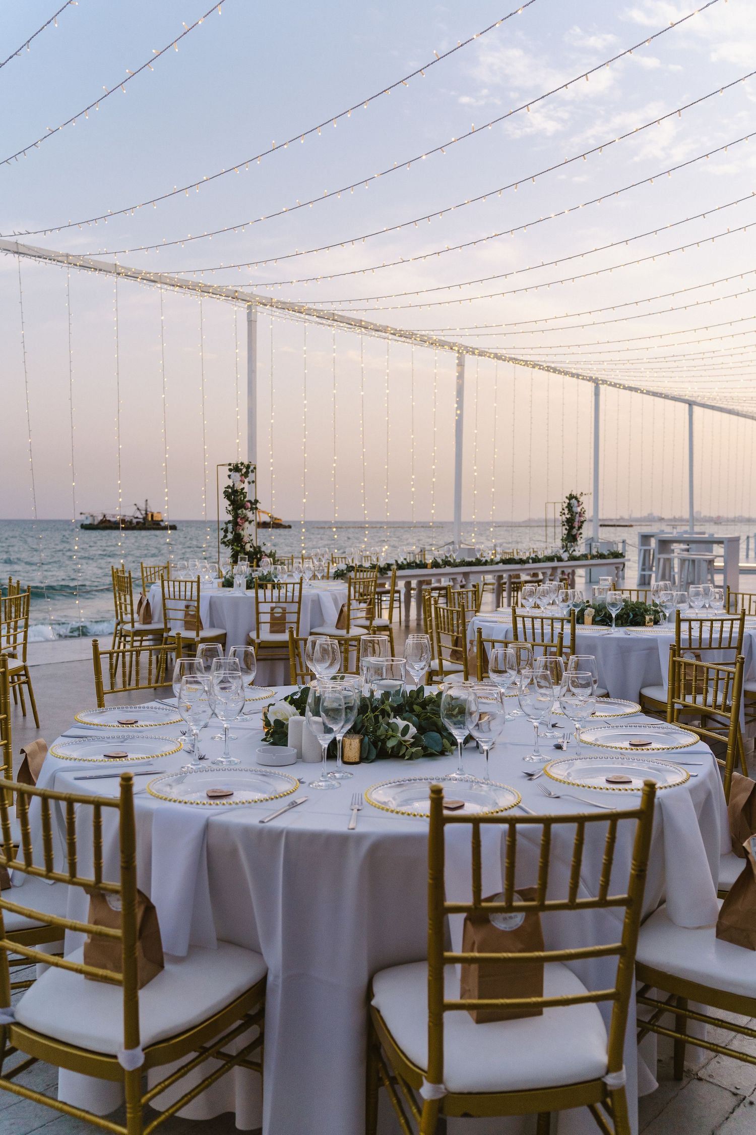 Elegant outdoor wedding reception setup with gold chiavari chairs and white linens overlooking the ocean.