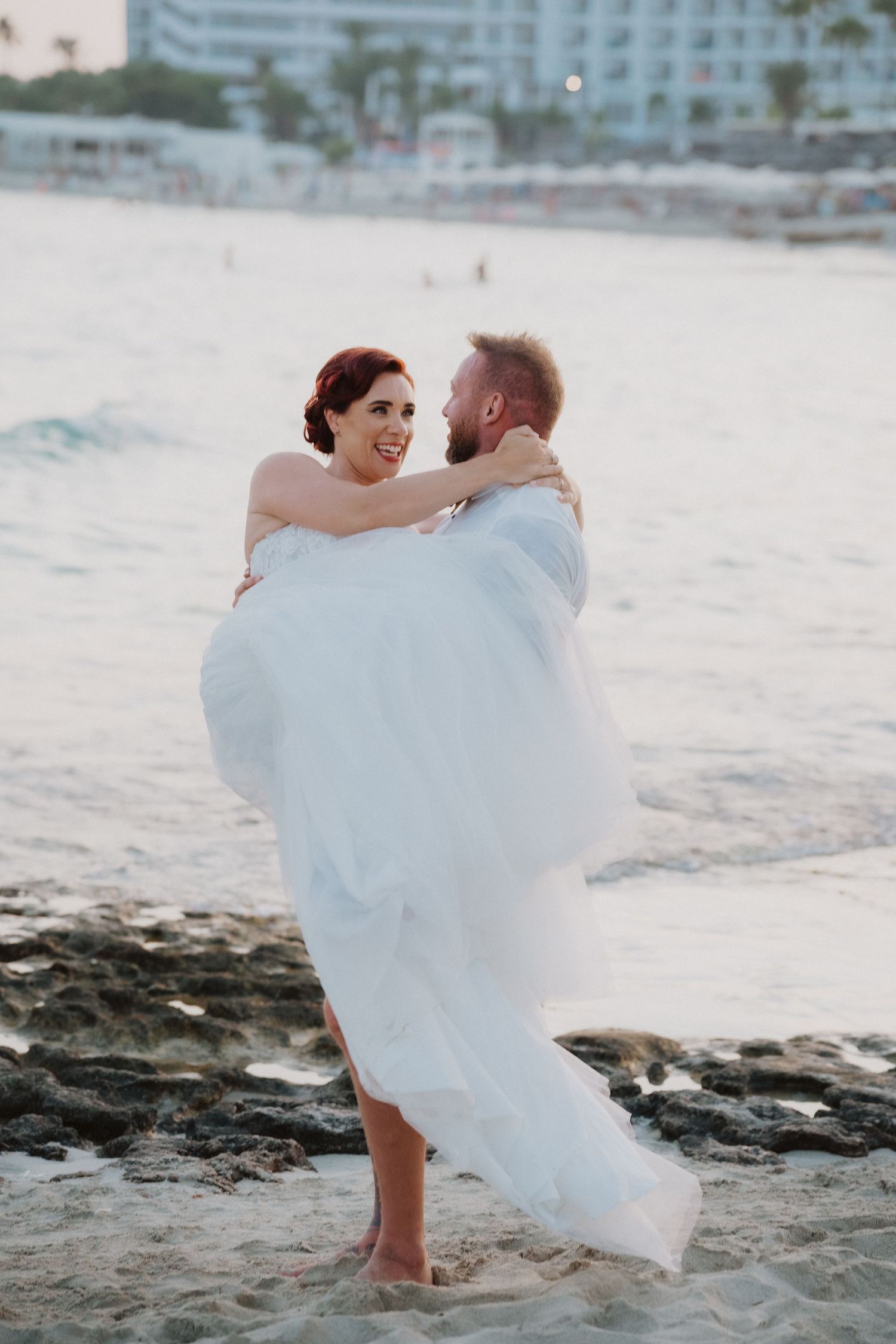 Beach wedding couple embracing on sandy shore at dusk.