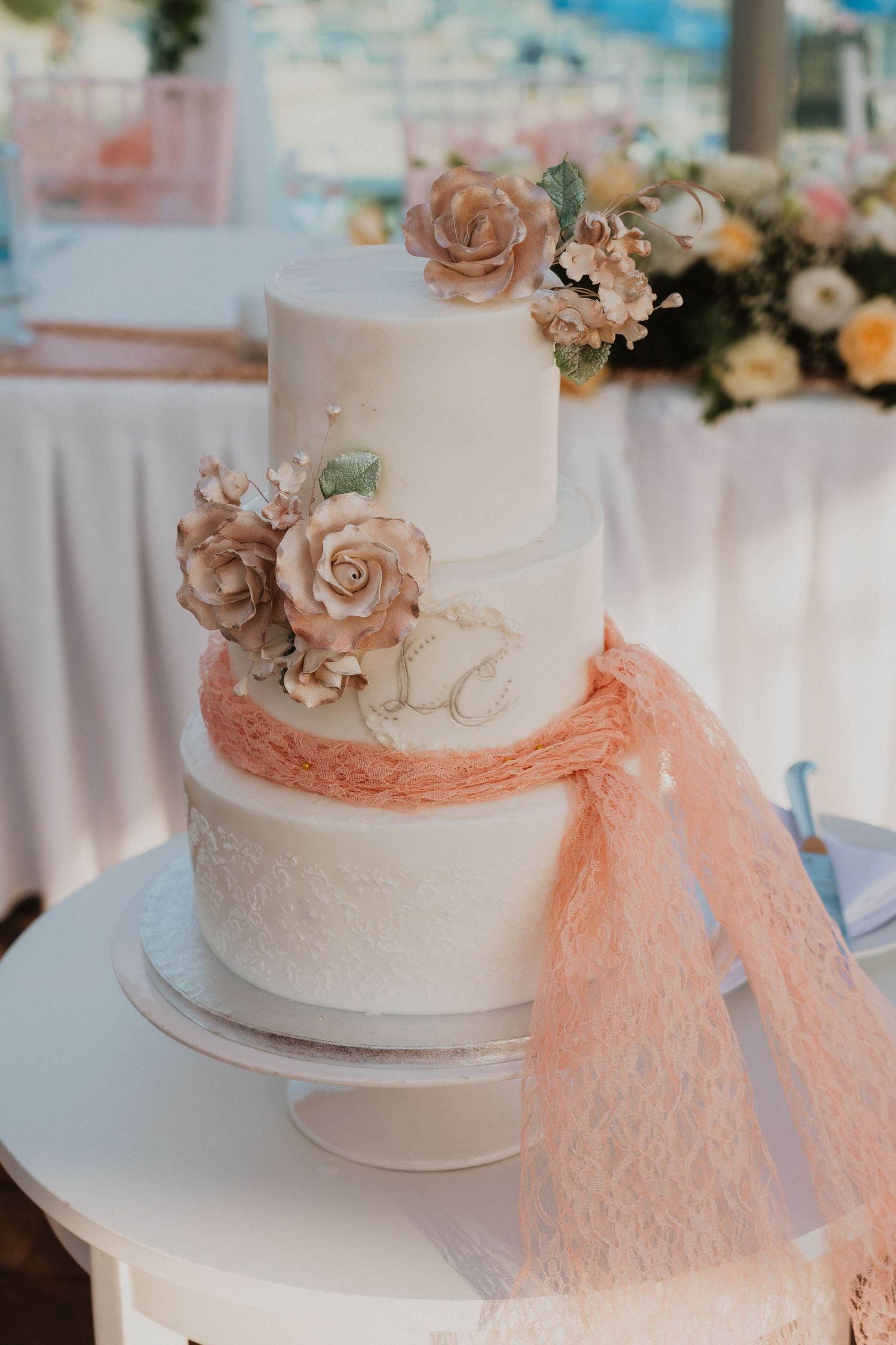 Three-tier white wedding cake decorated with blush roses and peach tulle ribbon.