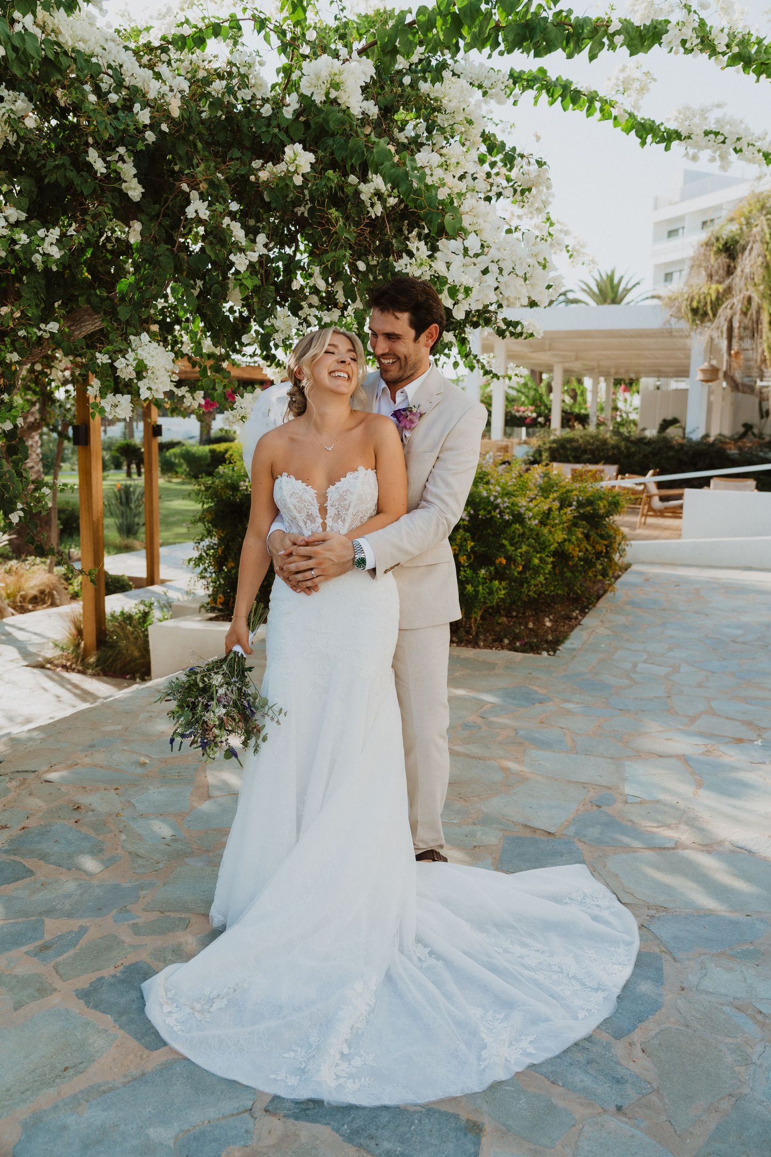 Wedding couple poses under hanging vines on stone pathway with flowing white dress.