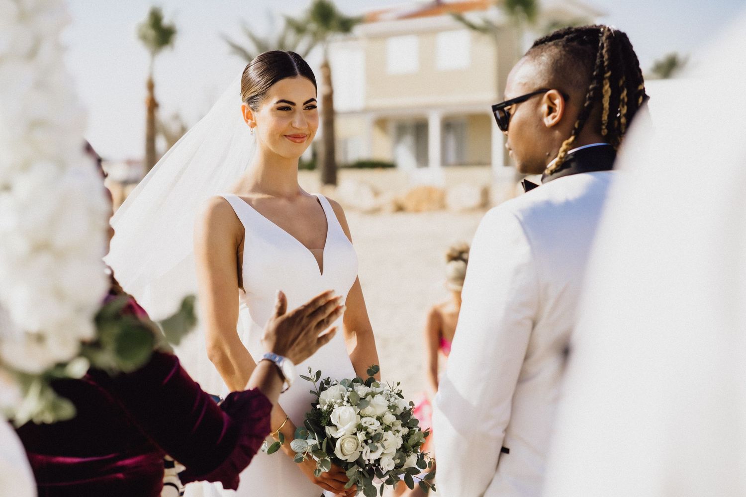 Joyful ceremony moment on a beach with palm trees and white floral decorations.