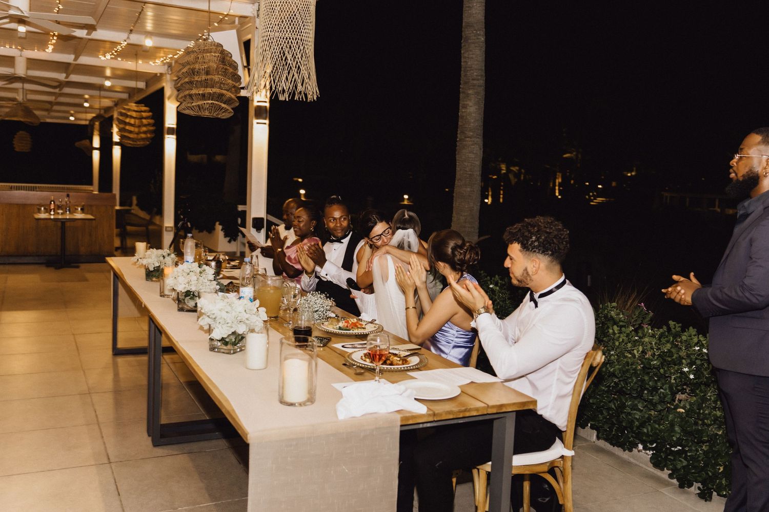 Wedding reception dinner with guests seated at a long table under string lights.