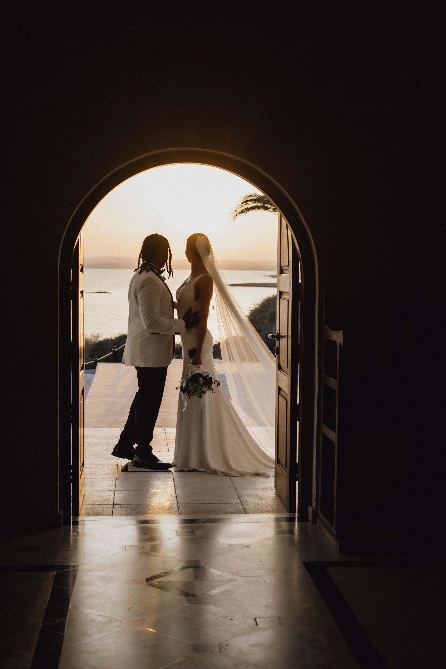 Silhouetted newlyweds share an intimate moment in an arched doorway at sunset.