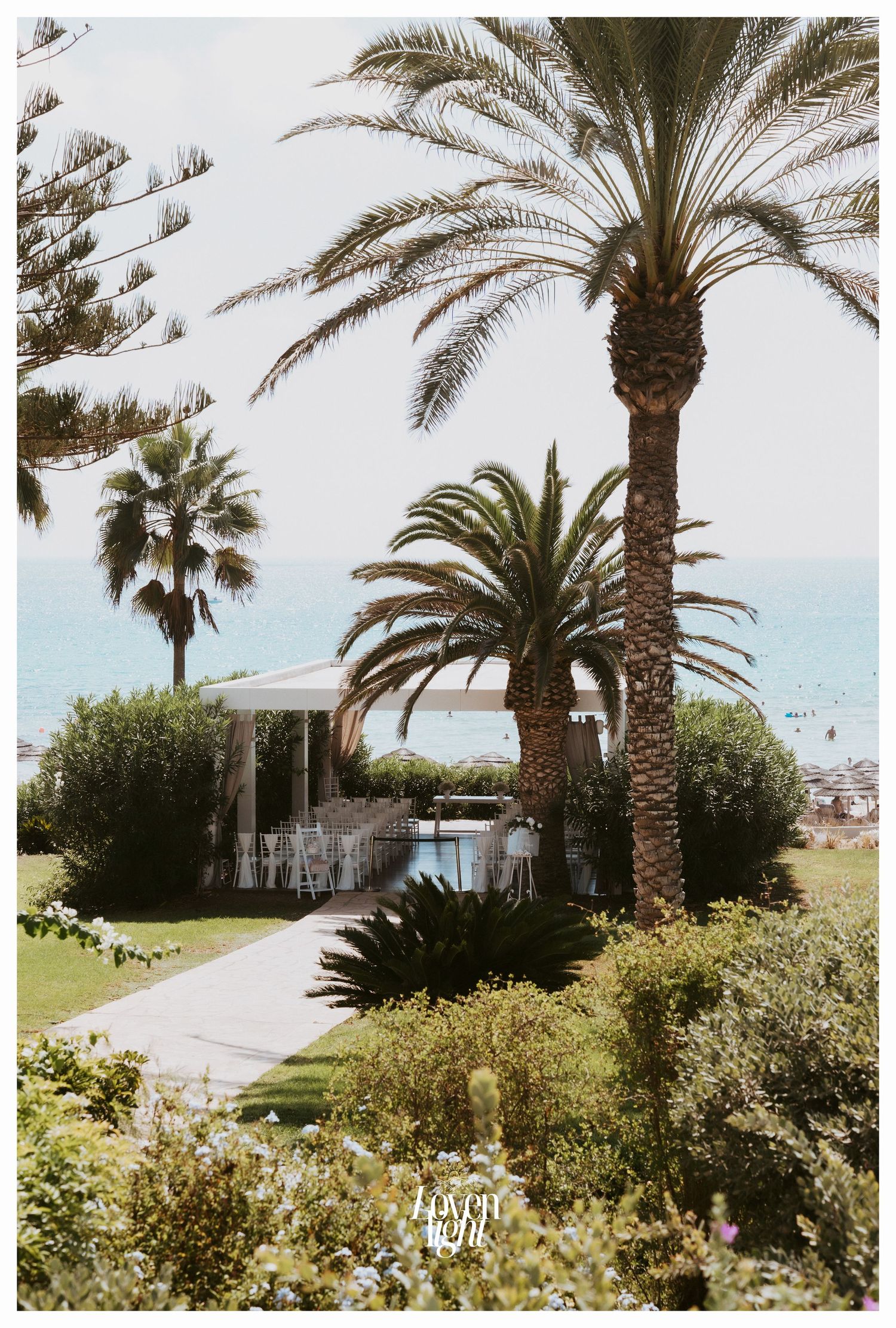 Tropical garden path leading to a coastal wedding ceremony site with tall palm trees.