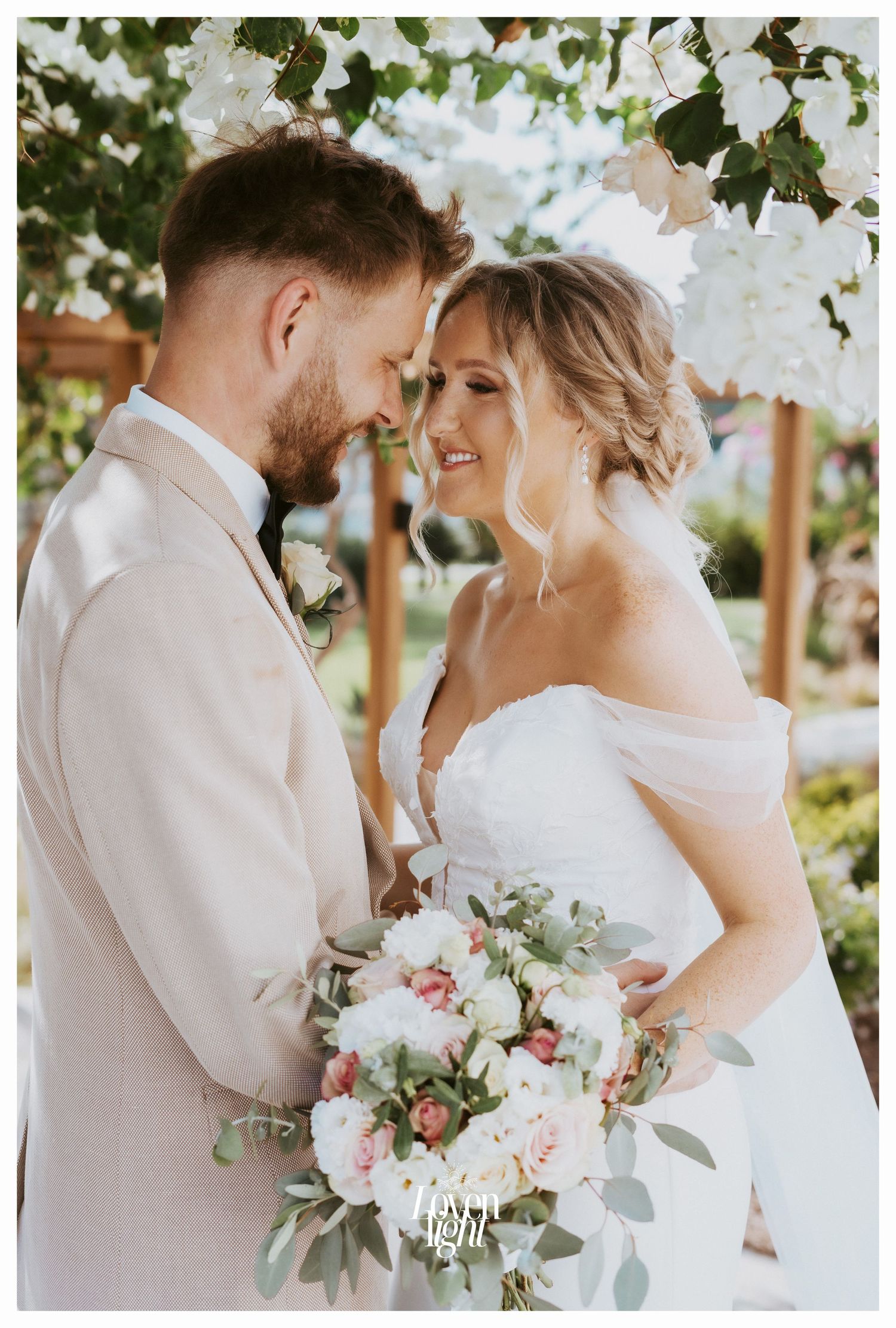 Intimate wedding portrait showing a tender moment between newlyweds with a soft pink and white floral bouquet.