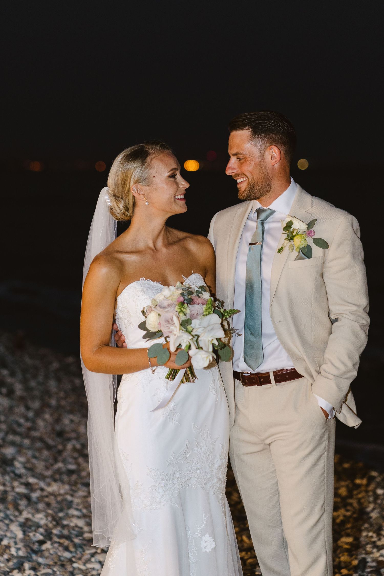 Couple shares a loving moment on a beach at night during their wedding celebration.