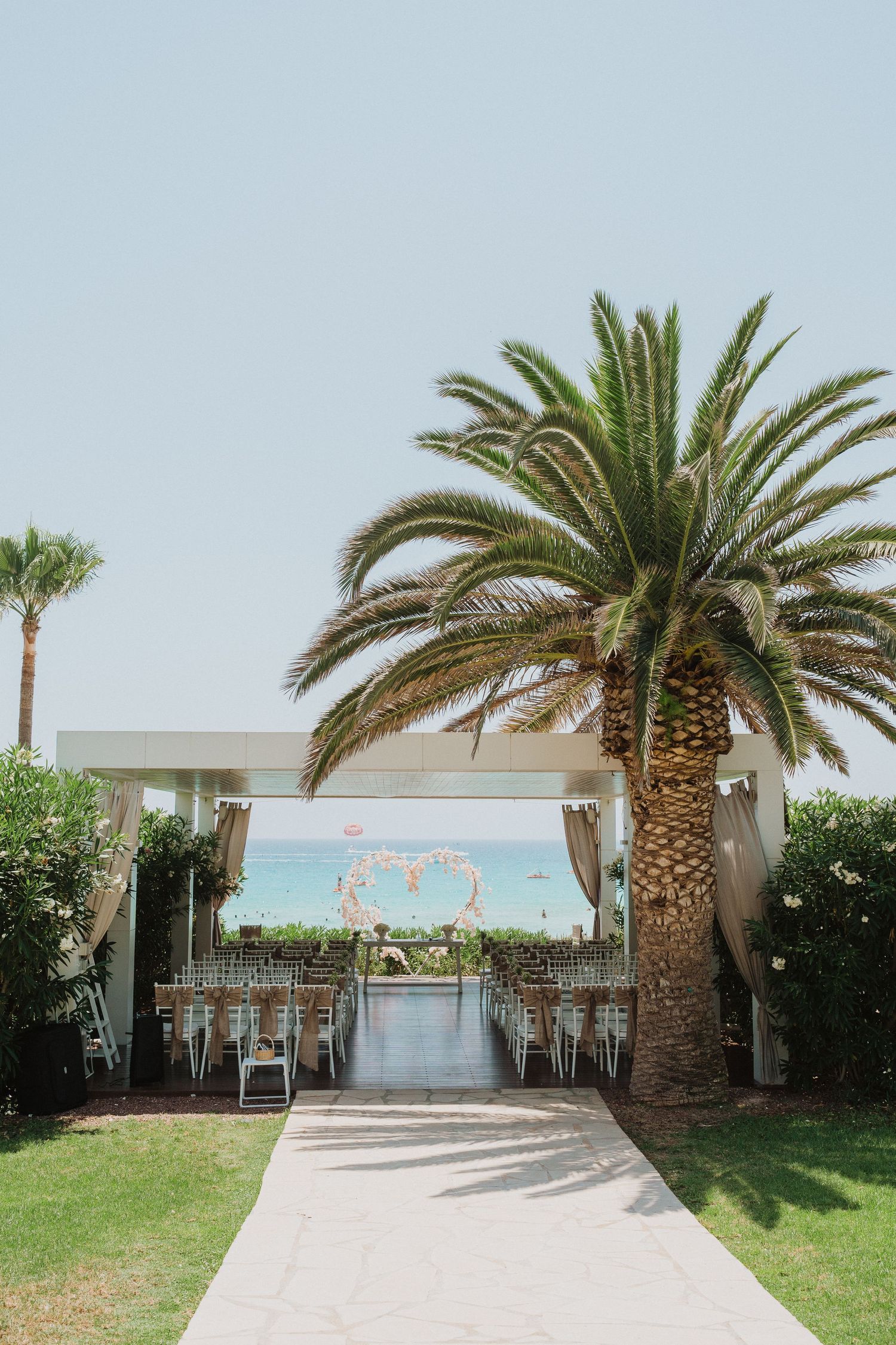 Wedding ceremony setup with palm trees framing a flower heart arch against ocean backdrop.