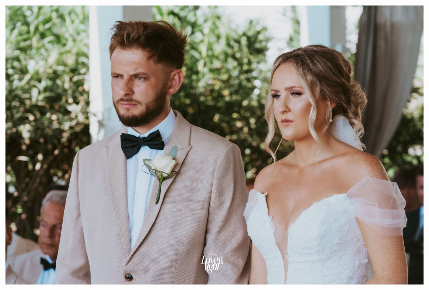 A wedding couple stands together during their outdoor ceremony in blush and white attire.