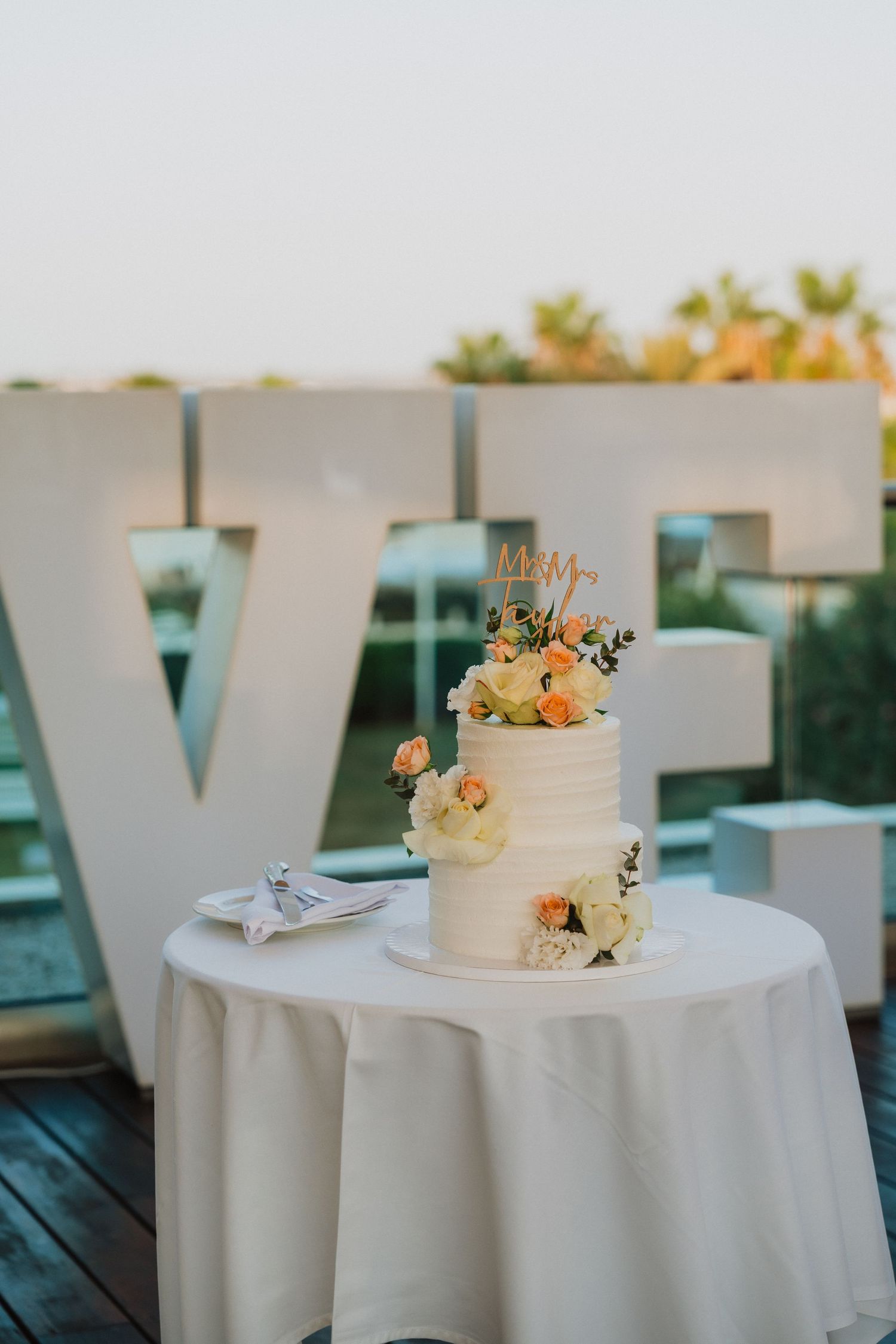 Elegant white wedding cake with floral decorations displayed on outdoor deck.