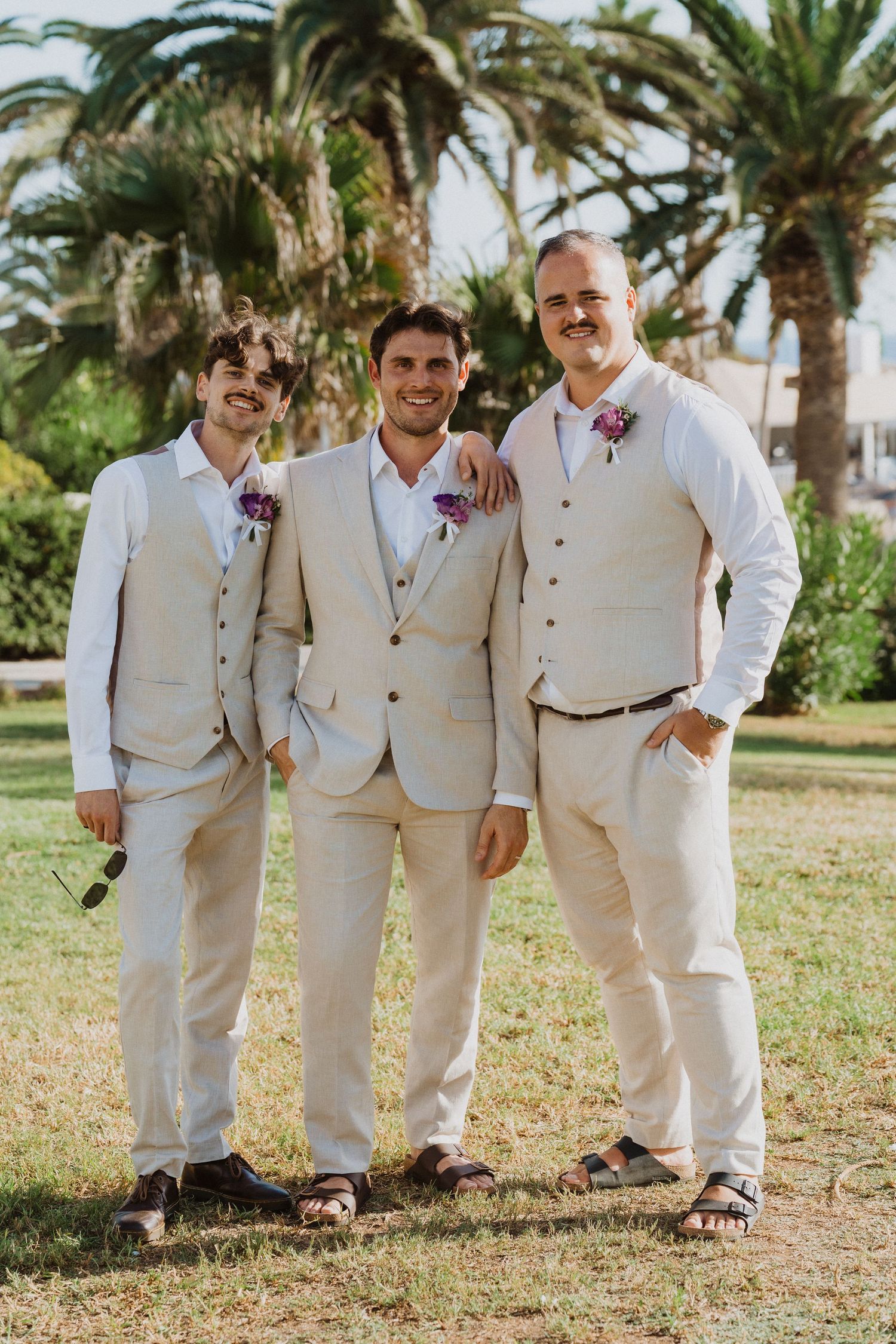 Young ring bearers in light colored suits pose together under palm trees.