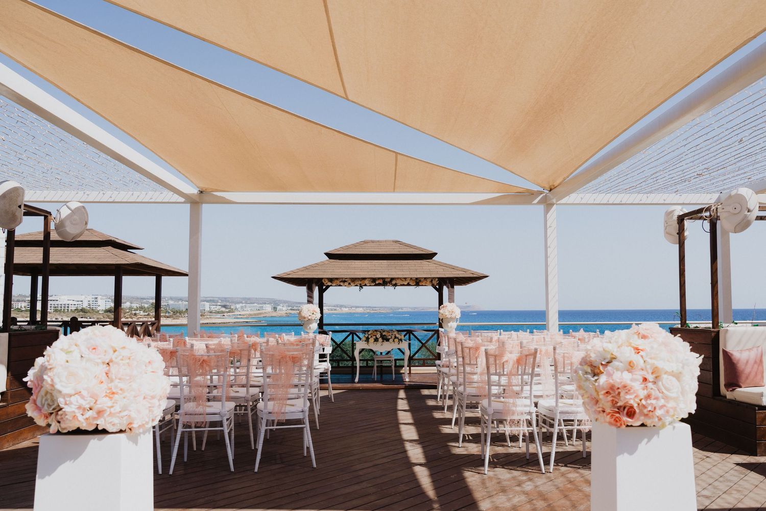 Beachside wedding venue with covered pavilions and rows of white chairs on a wooden deck.
