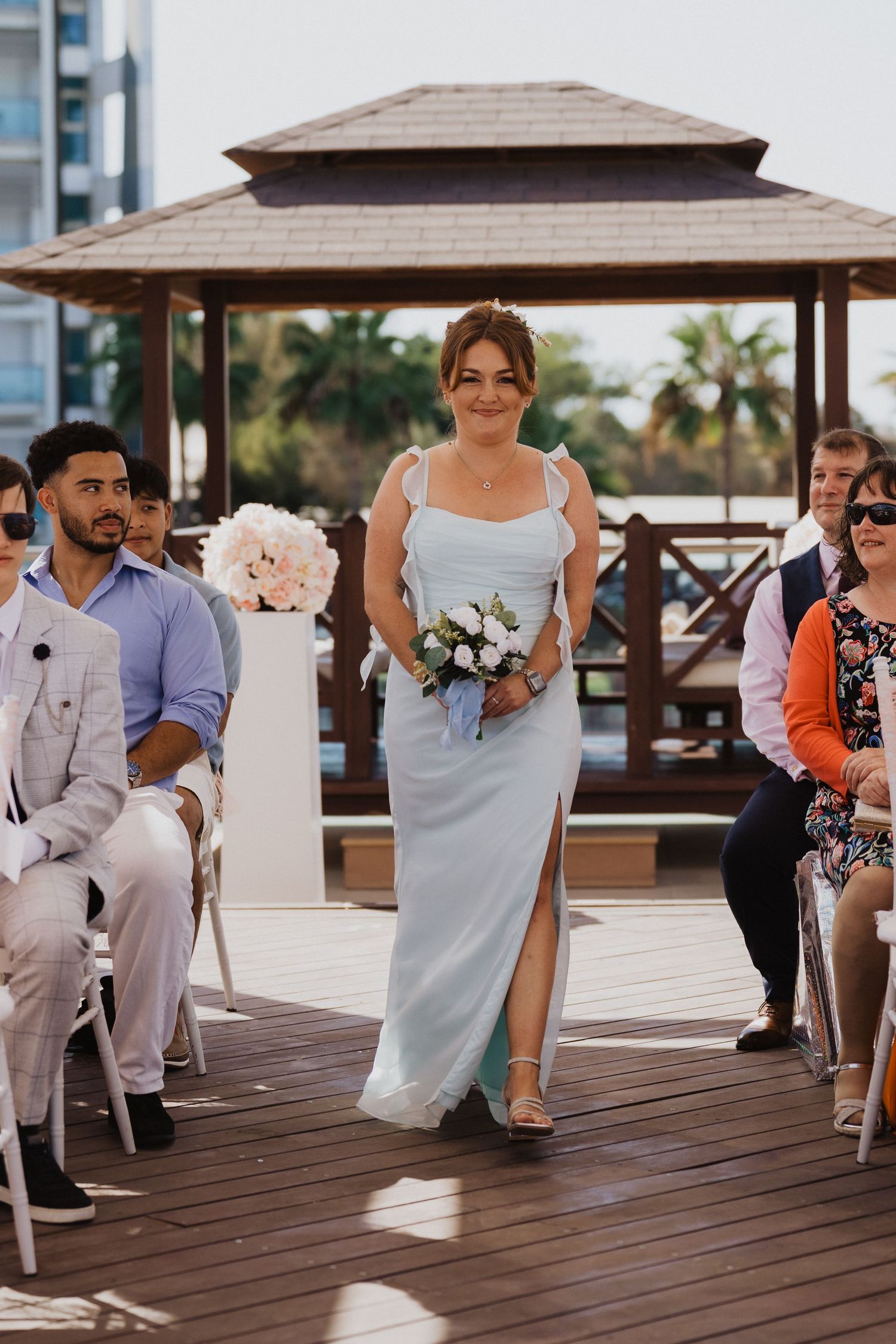 Wedding ceremony on a wooden deck with guests seated and bridesmaids walking down the aisle.