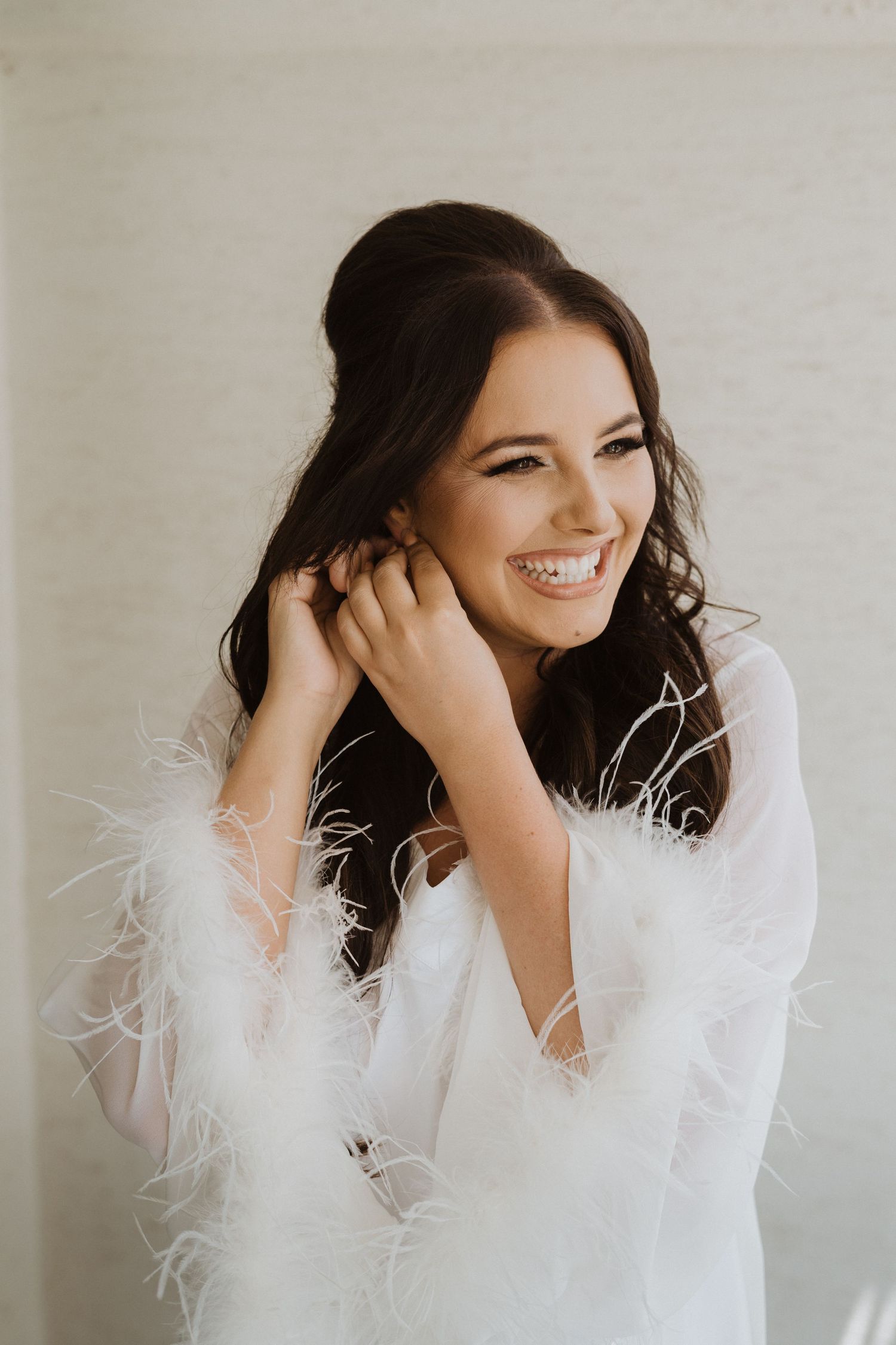 A joyful moment captured in white feathered robe during wedding preparations.
