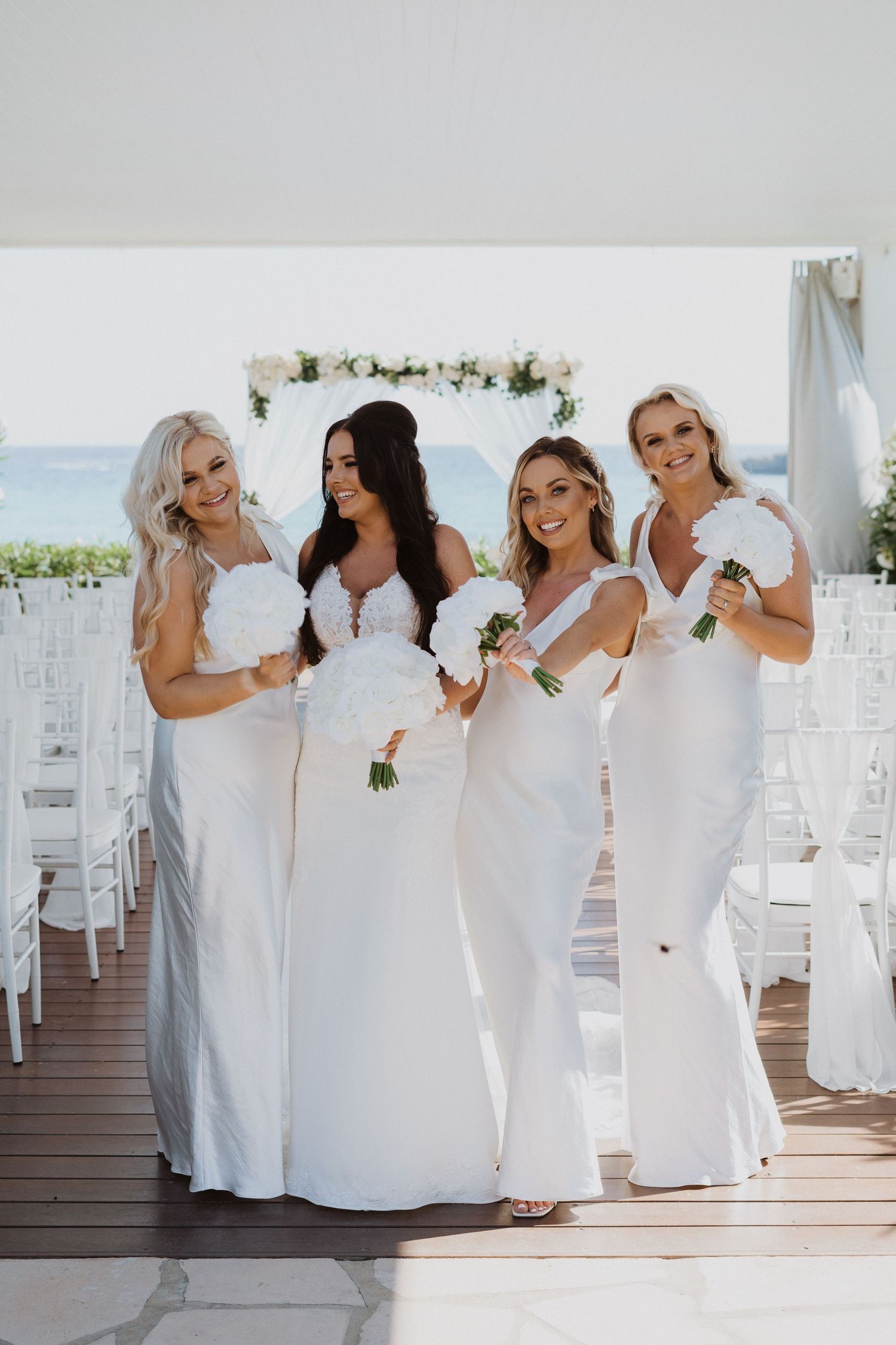 Bridesmaids in white dresses sharing a candid moment at an outdoor wedding venue.
