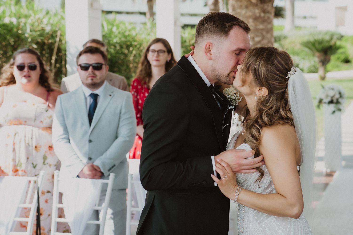 Newlyweds sharing their first kiss at an outdoor wedding ceremony with guests watching.