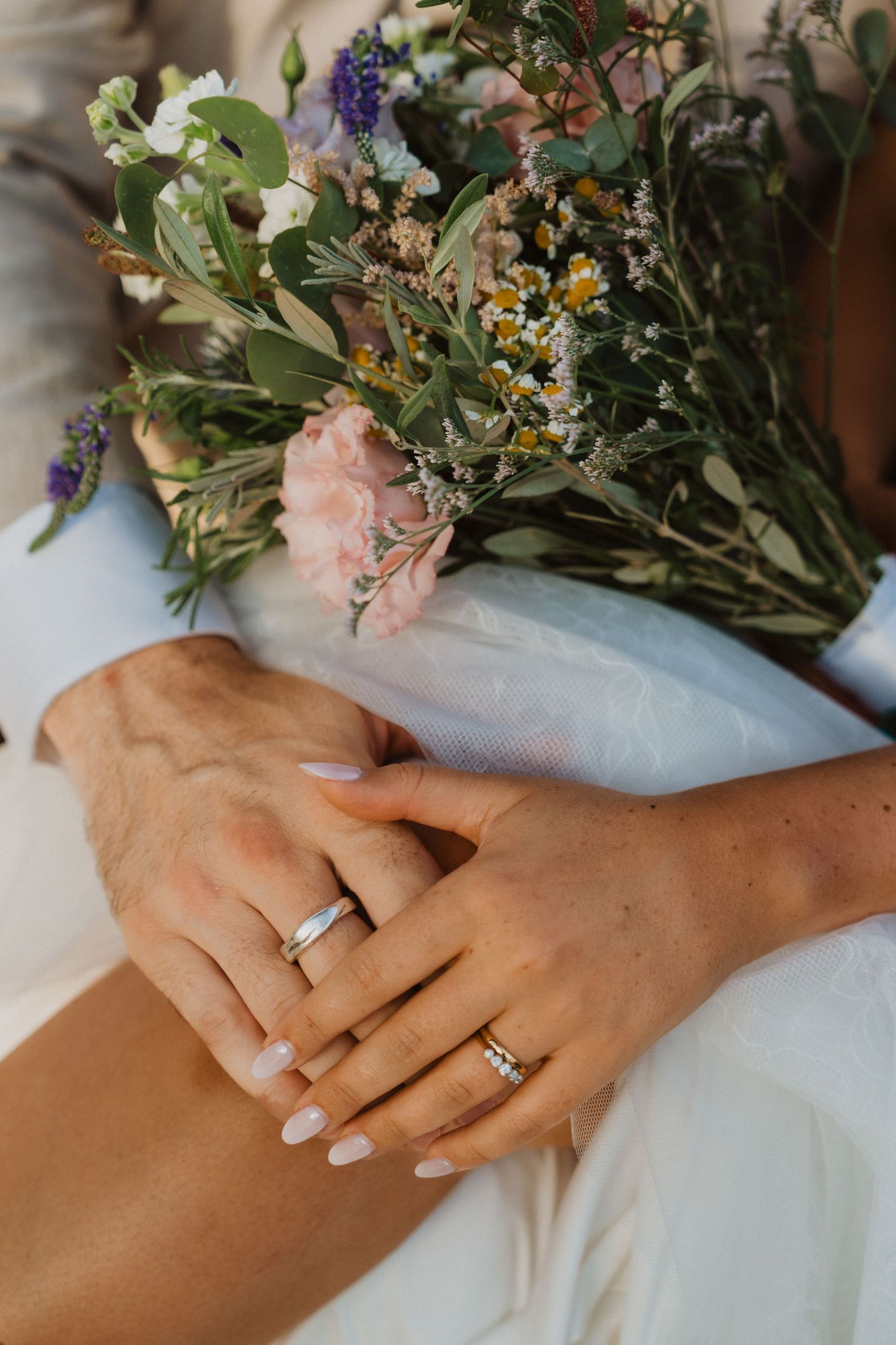 Close-up of hands with wedding rings next to a delicate wildflower bouquet.