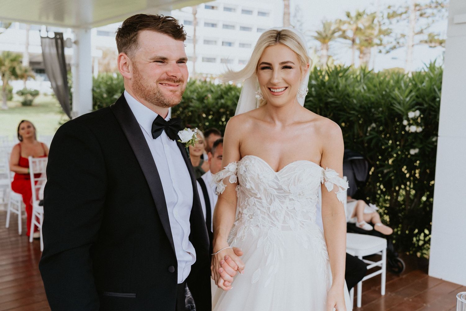 A newlywed couple share a joyful moment on their wedding day at a coastal venue.