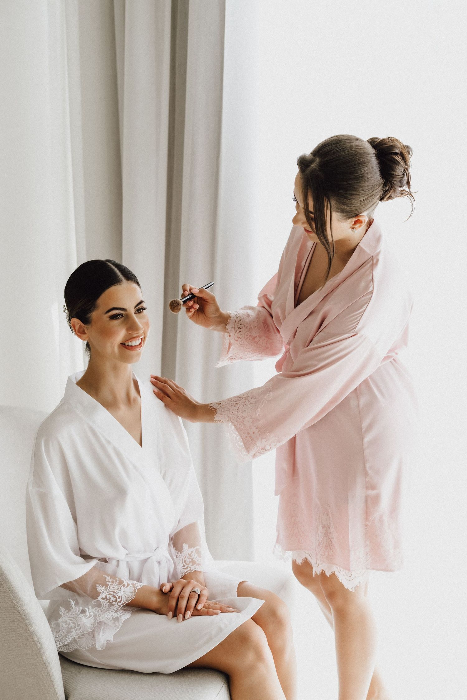 A makeup artist styles a woman's hair as she sits in a white robe.