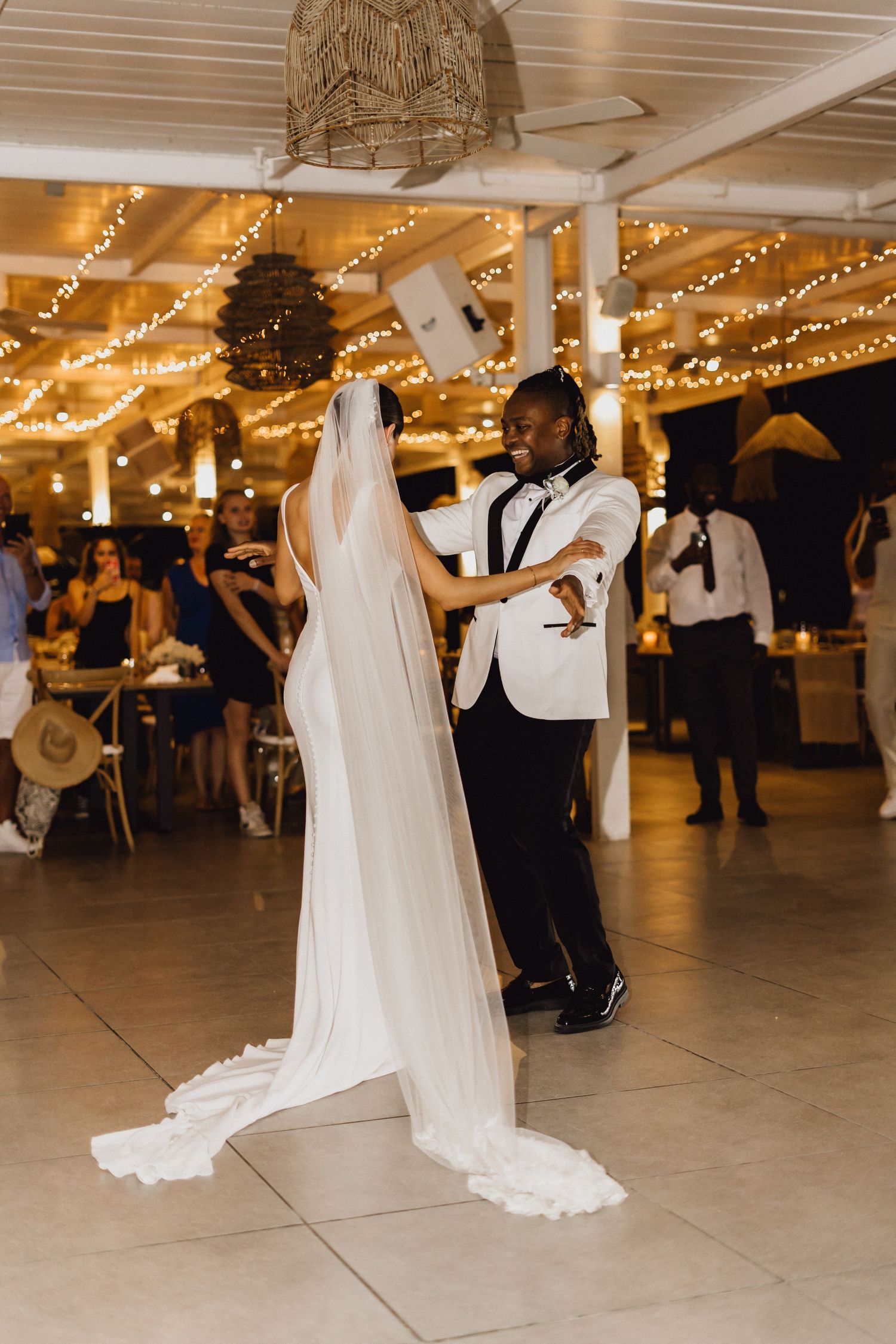 A couple shares their first dance together at an indoor wedding reception under twinkling lights.