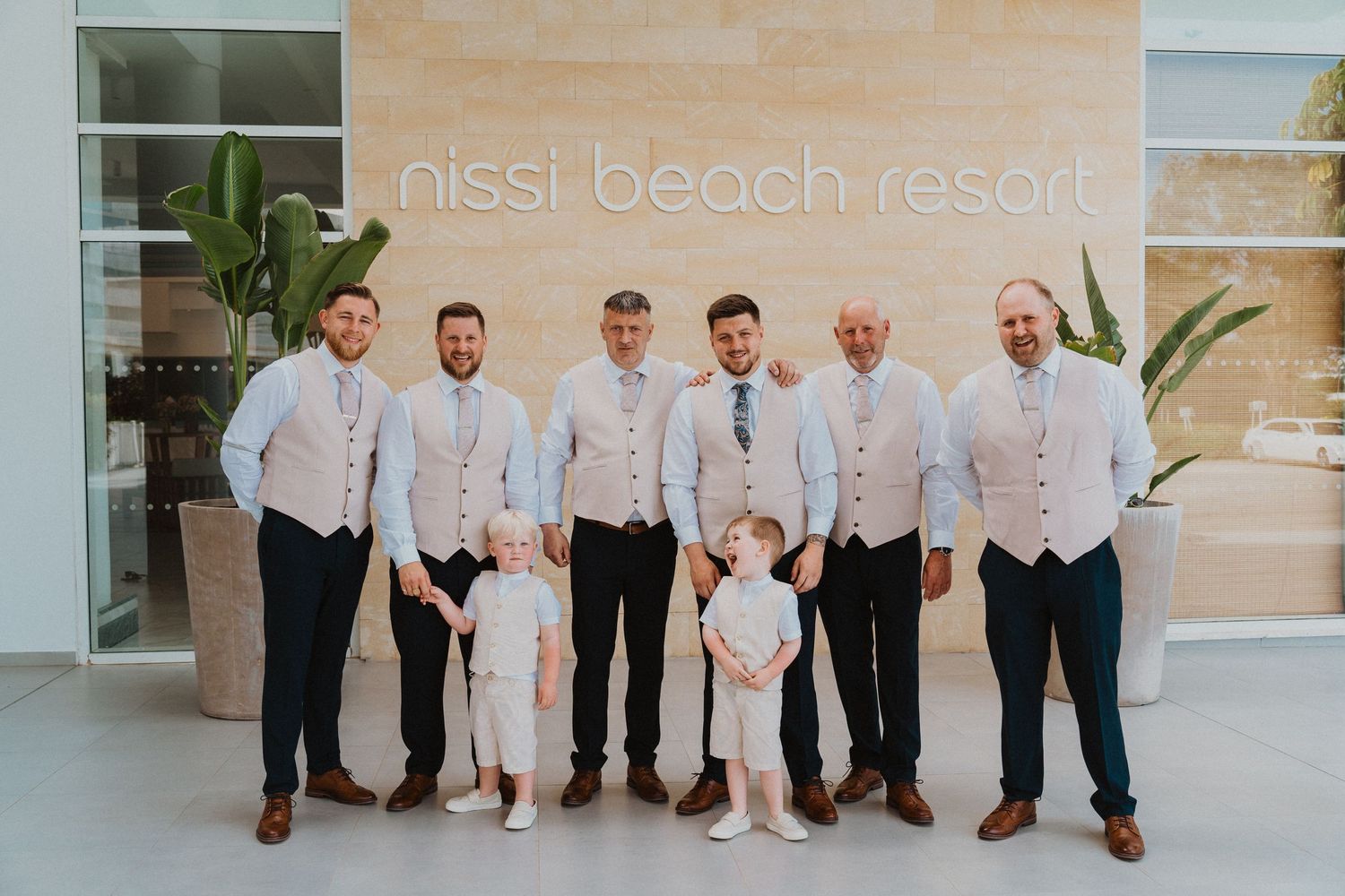 Group photo of wedding party members in matching attire at beach resort entrance.