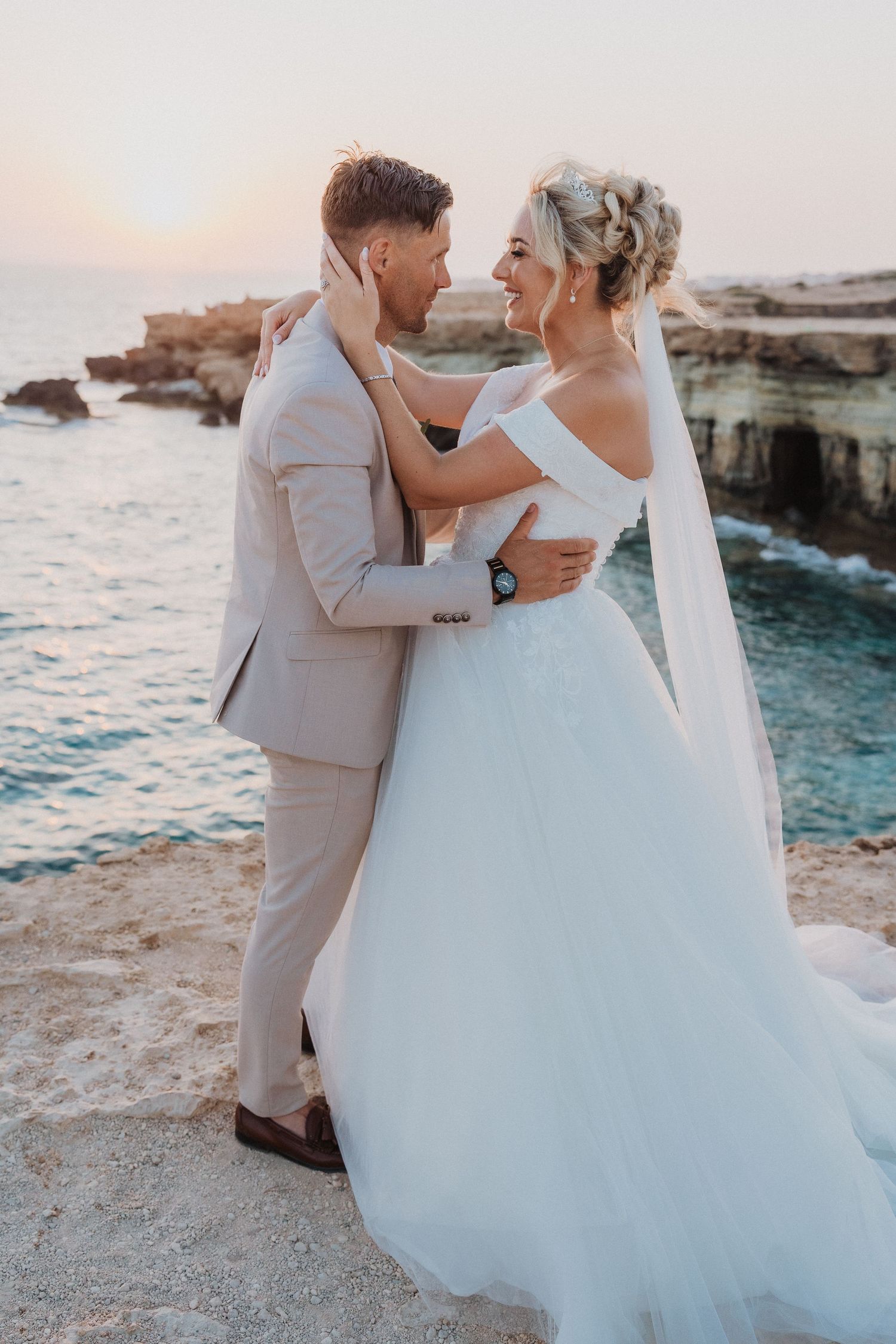Romantic sunset wedding portrait on coastal cliffs with flowing white dress and light colored suit.
