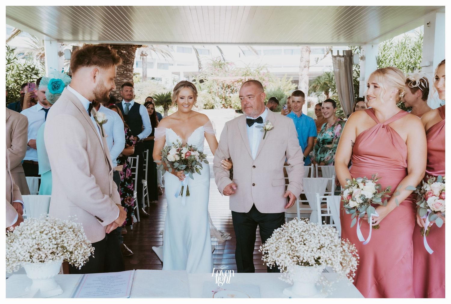 Wedding ceremony with bridal party in coral dresses and beige suits.