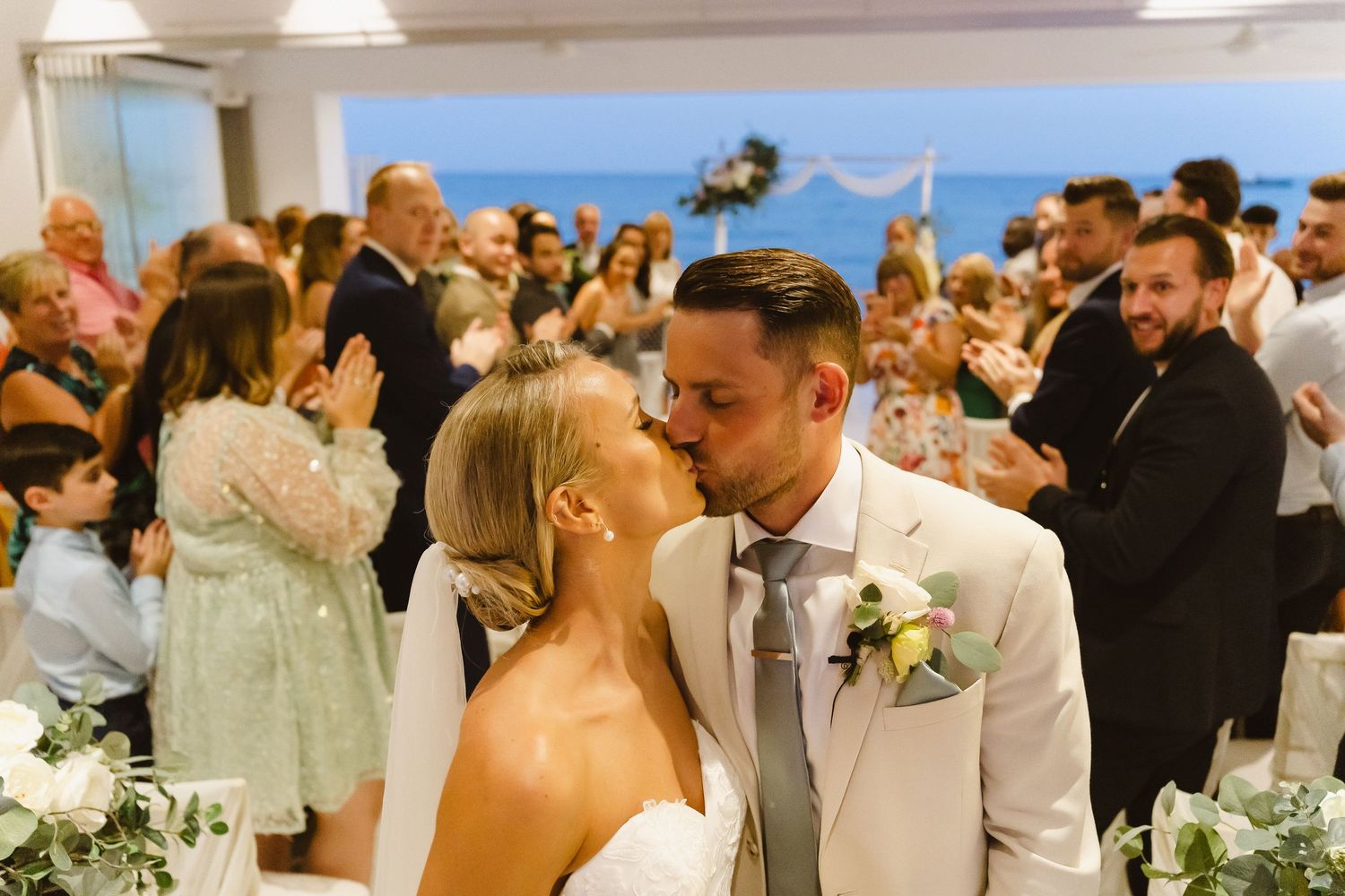 A tender moment between newlyweds as guests celebrate in the background at a wedding reception.