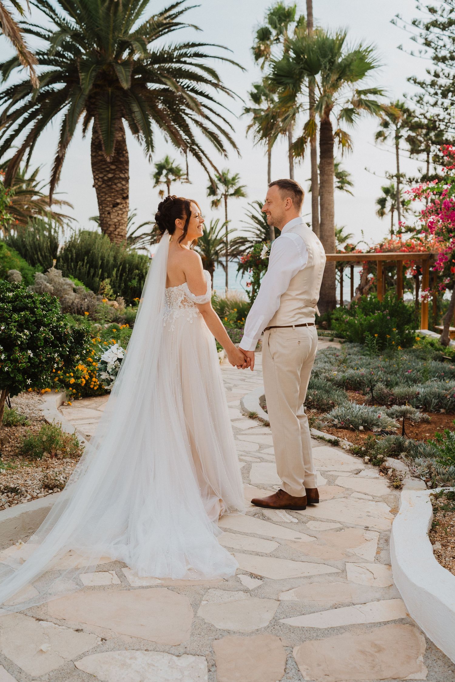 A tropical wedding ceremony on a stone path with palm trees and bougainvillea flowers in the background at sunset.