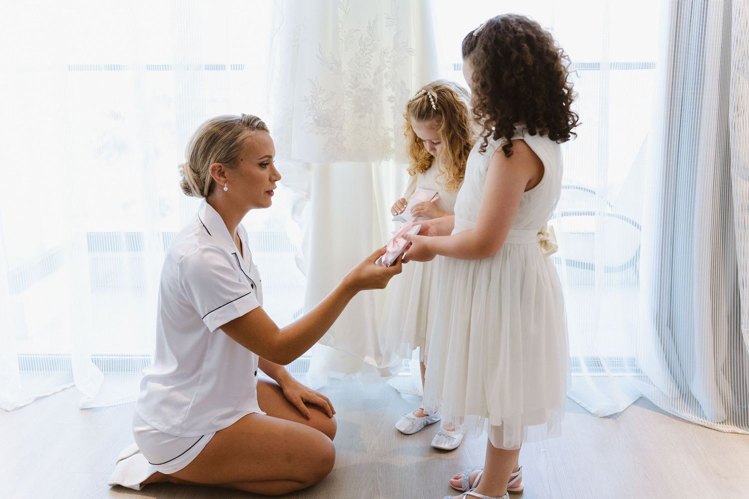 Tender moment between woman and child in white dresses during wedding preparations.