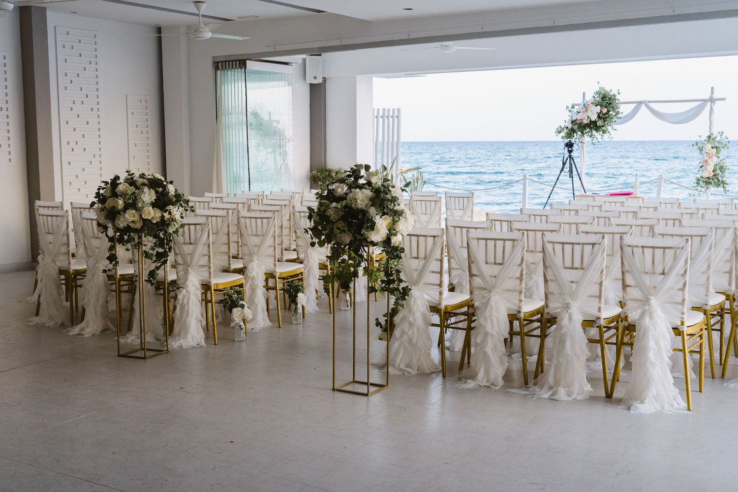 Oceanfront wedding ceremony setup with white chairs and floral arrangements.