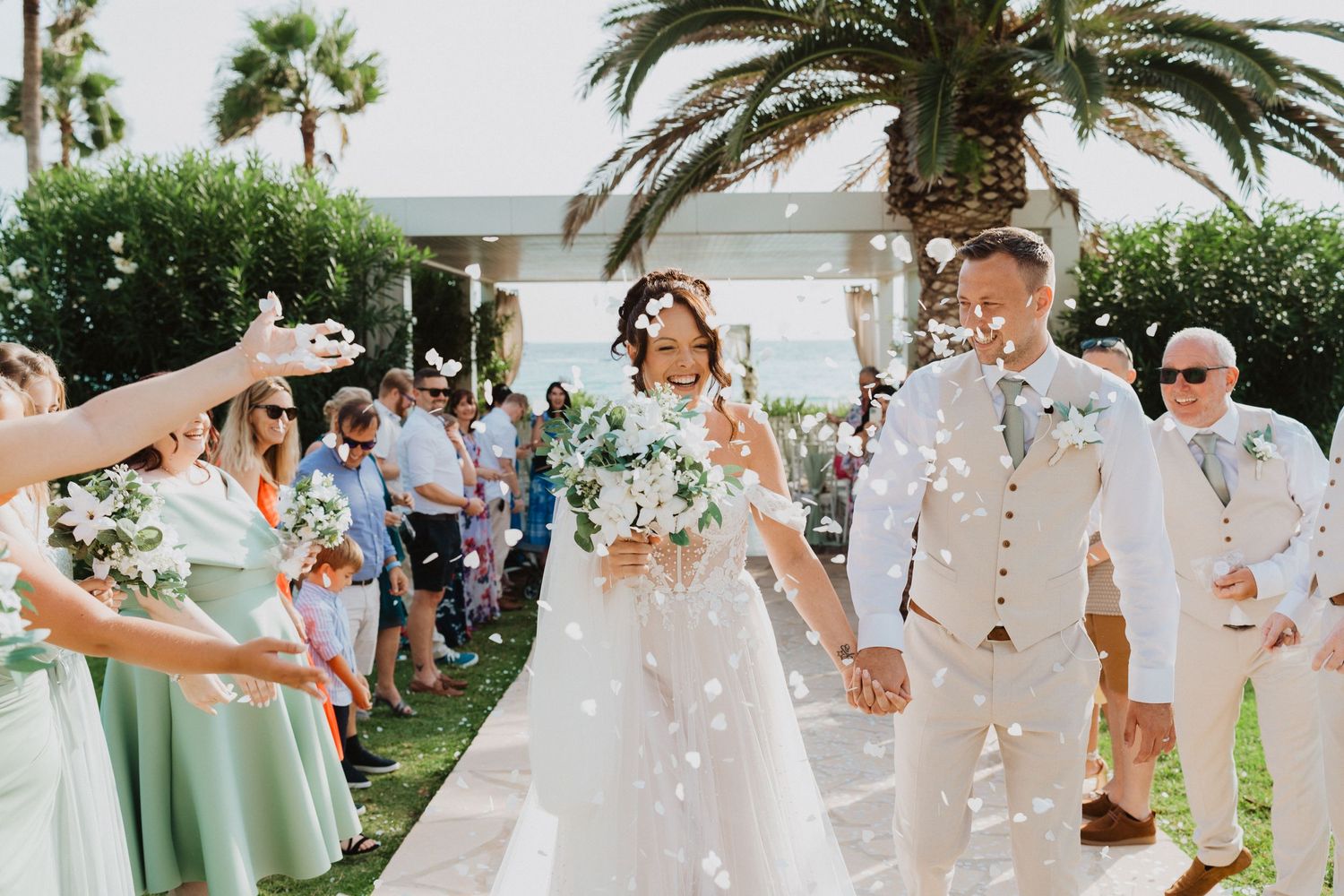 Joyful wedding celebration with guests throwing flower petals at a tropical outdoor ceremony.