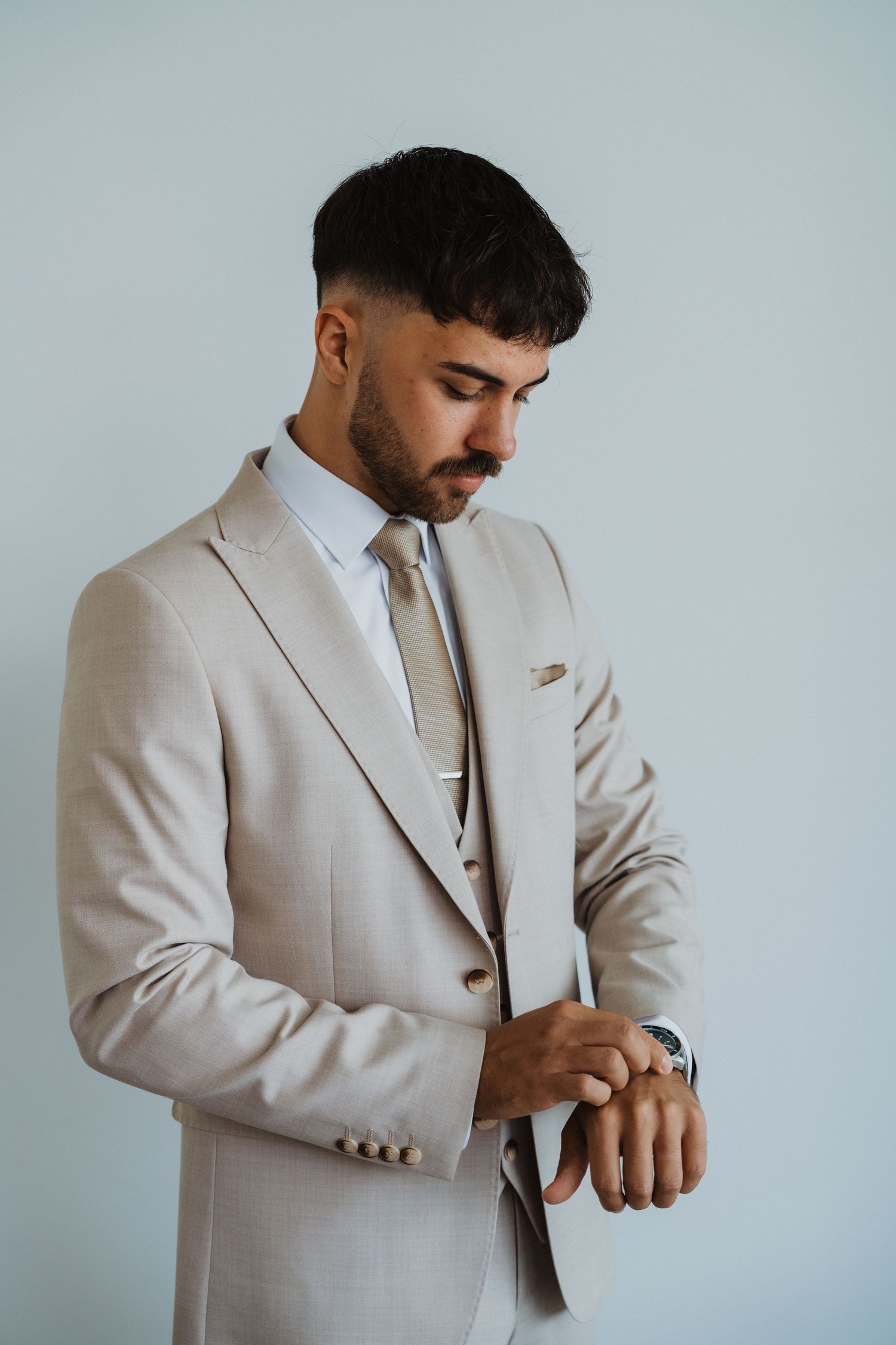 Groom checking his watch and adjusting suit details before ceremony.