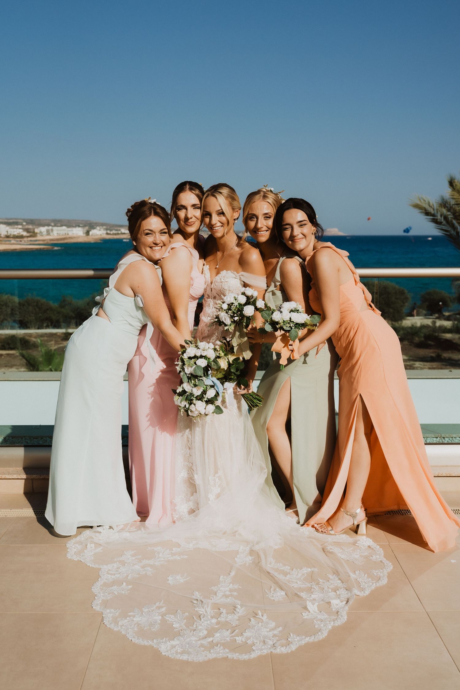 Wedding party in pastel colors poses together with ocean views.