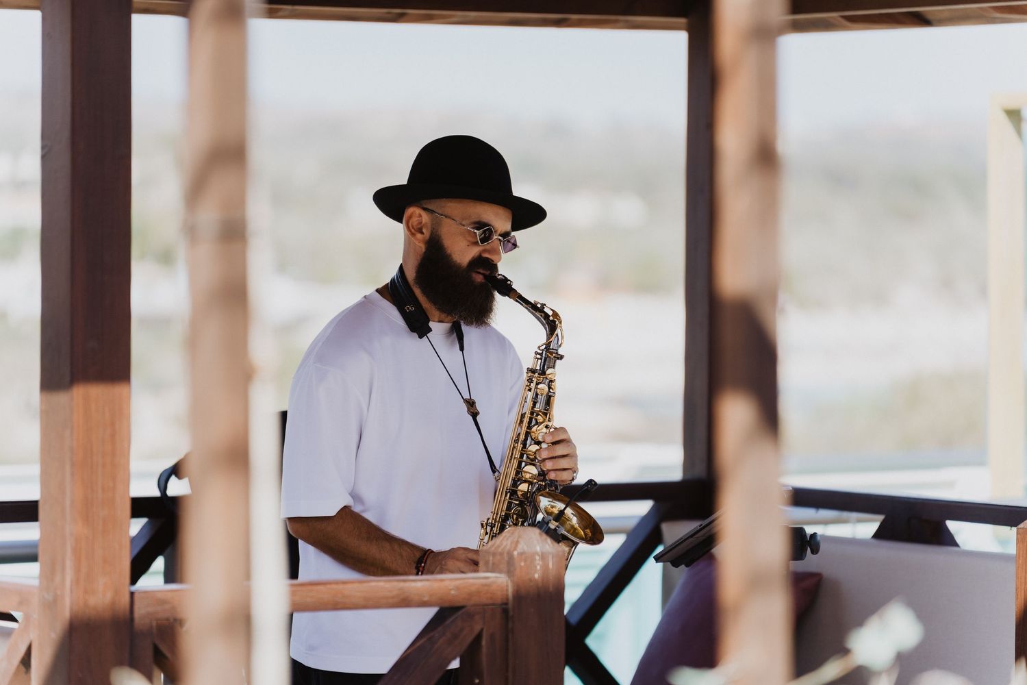 Jazz musicians perform live music at an outdoor venue with wooden beams and shade sails overhead.