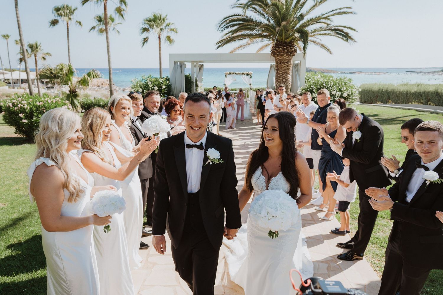 Wedding celebration with formal attire and palm trees along a beachfront venue.