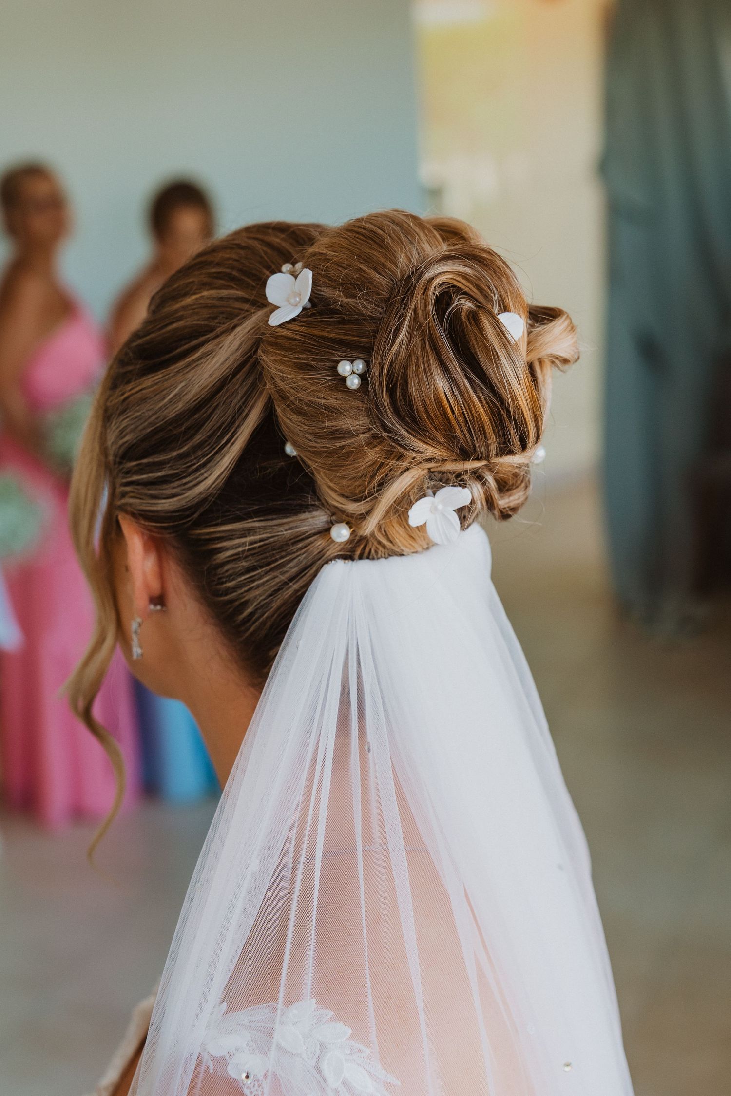 A bridal hairstyle shown from different angles featuring an elegant updo with a flowing white veil and delicate floral accents.