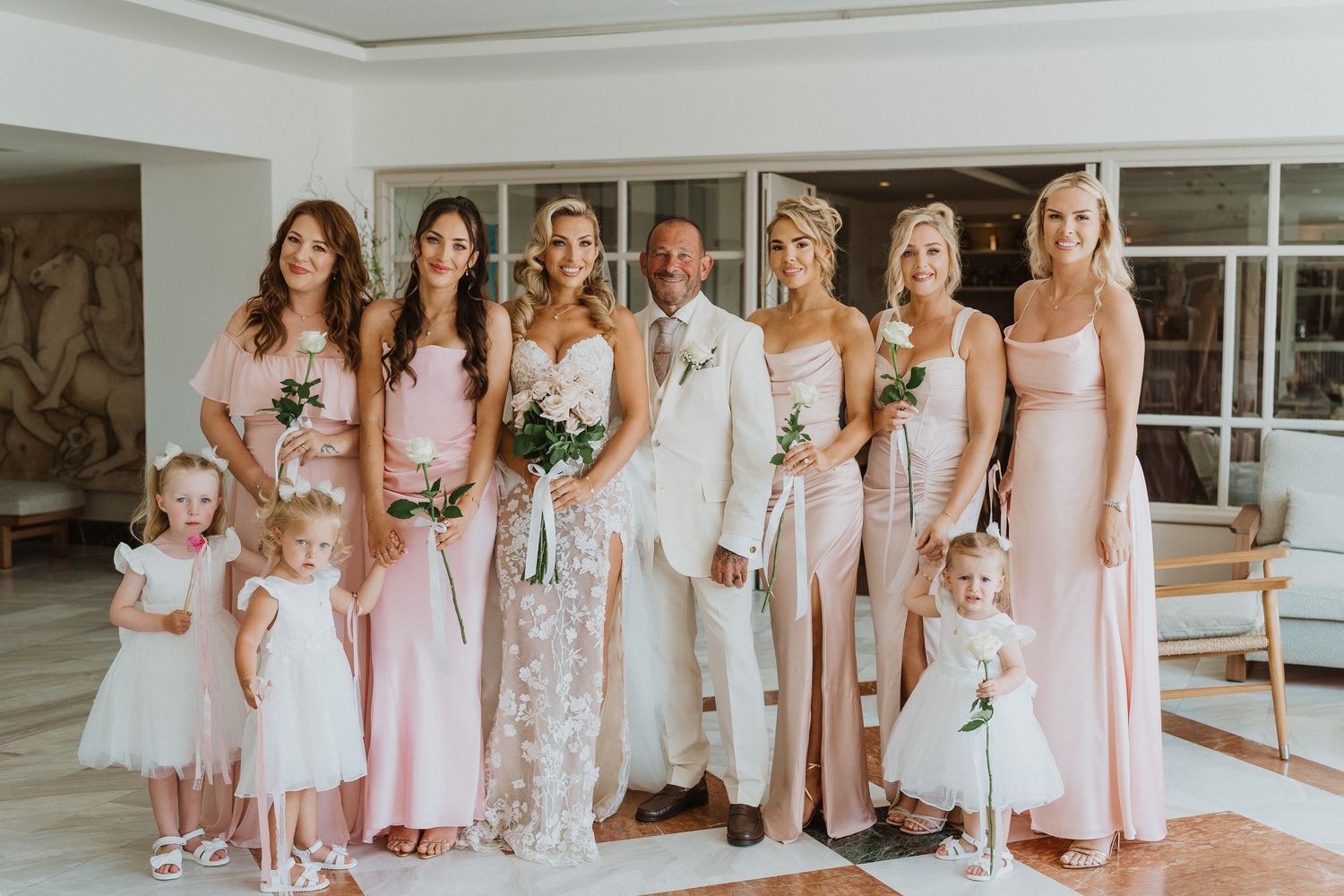 A group wearing coordinated pink and blush dresses stands together in an elegant bridal party photo shoot.