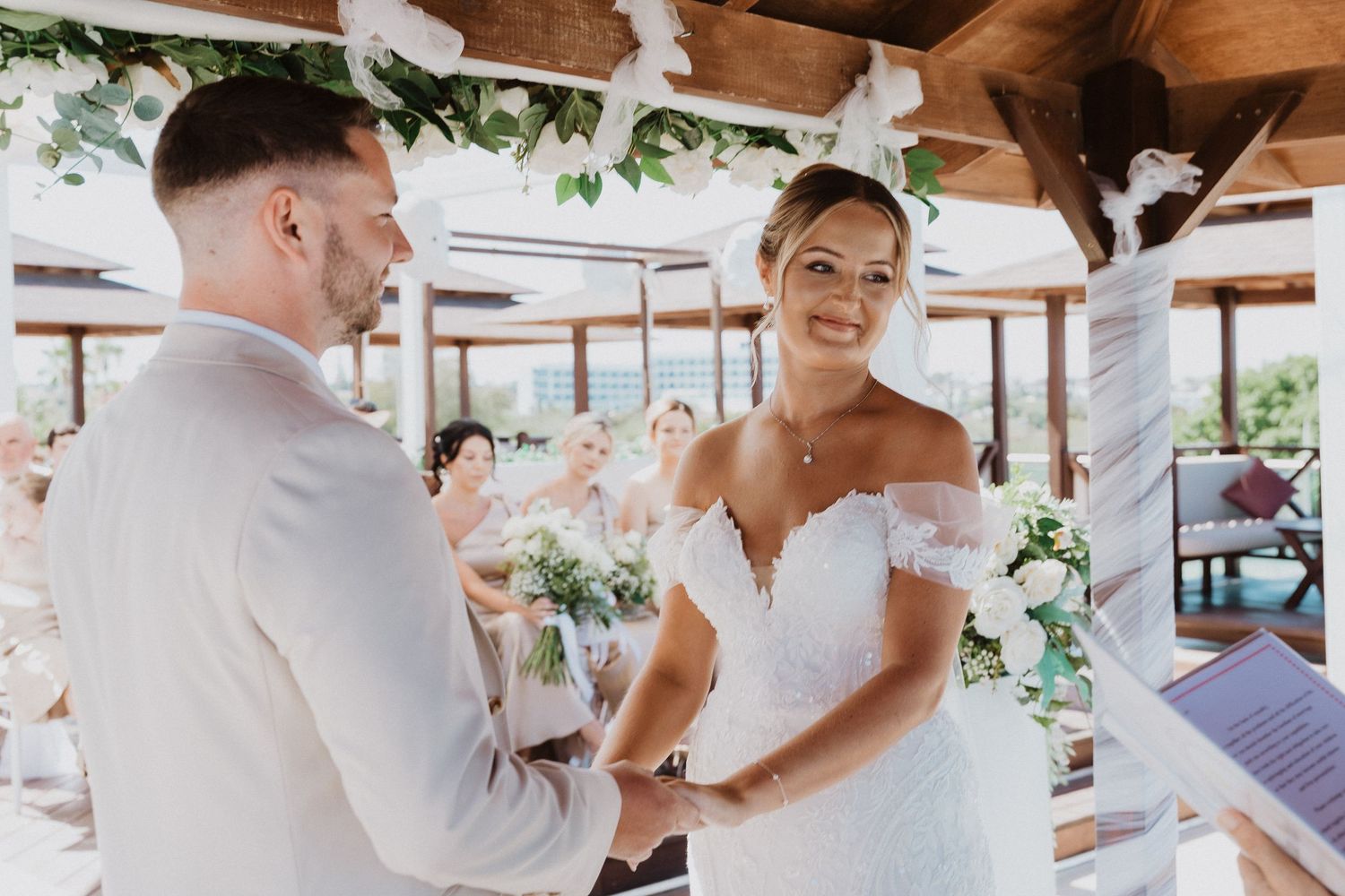 Wedding couple shares a tender moment during their first dance at an outdoor reception venue with wooden beams and greenery.