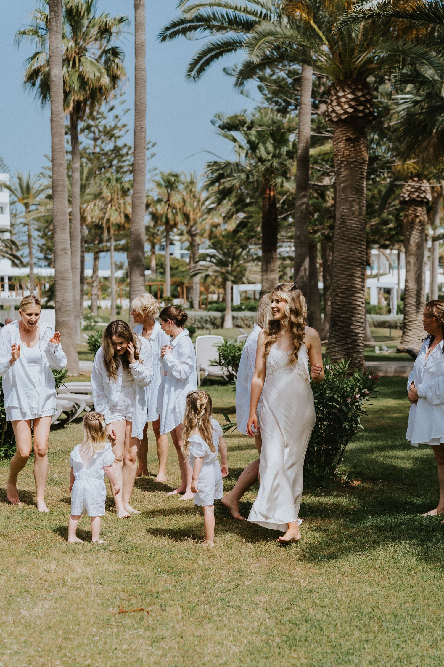 Group walking through a tropical palm garden wearing white and cream outfits.