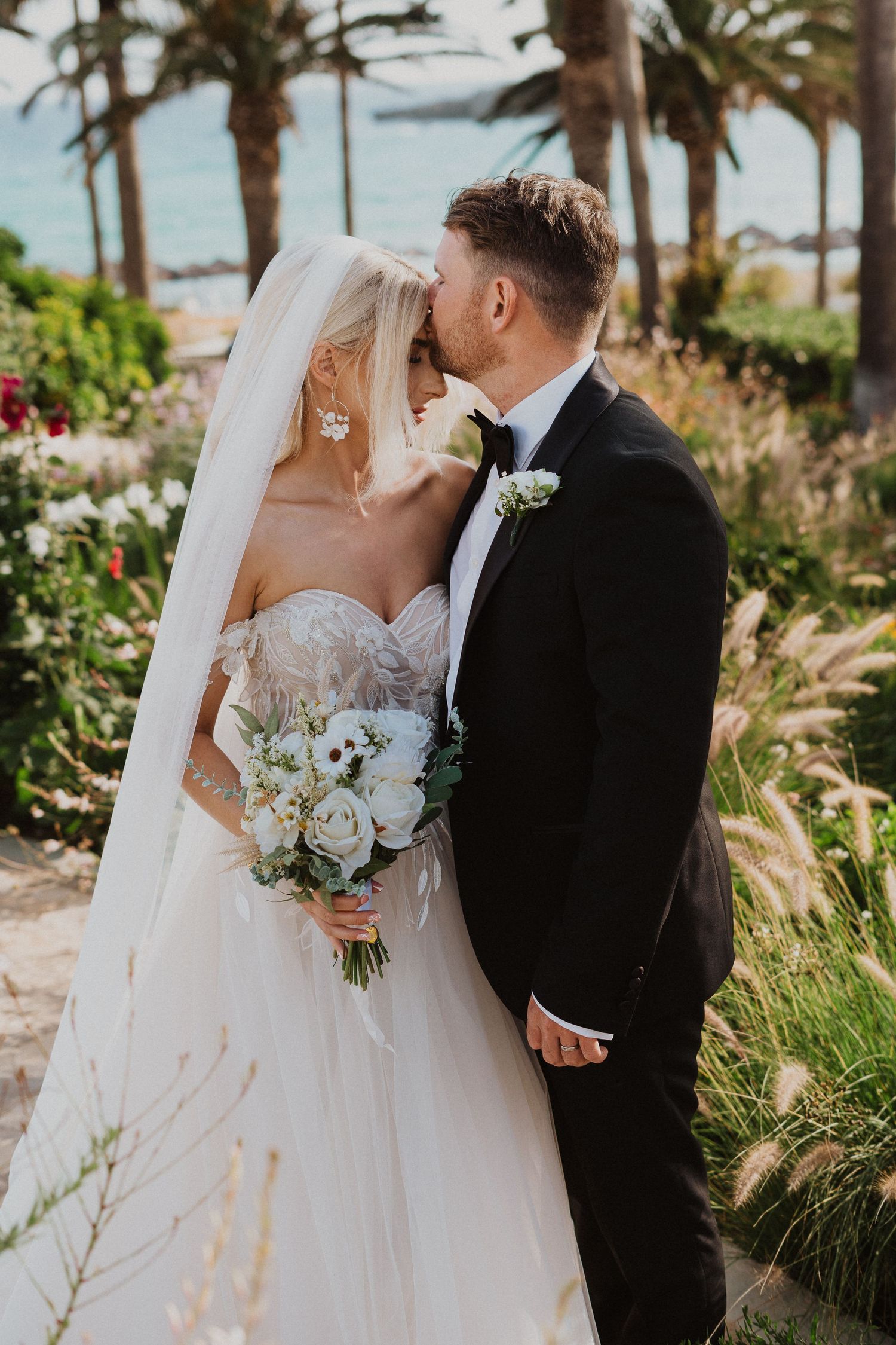 Intimate wedding portrait in a coastal garden with palm trees and white florals.