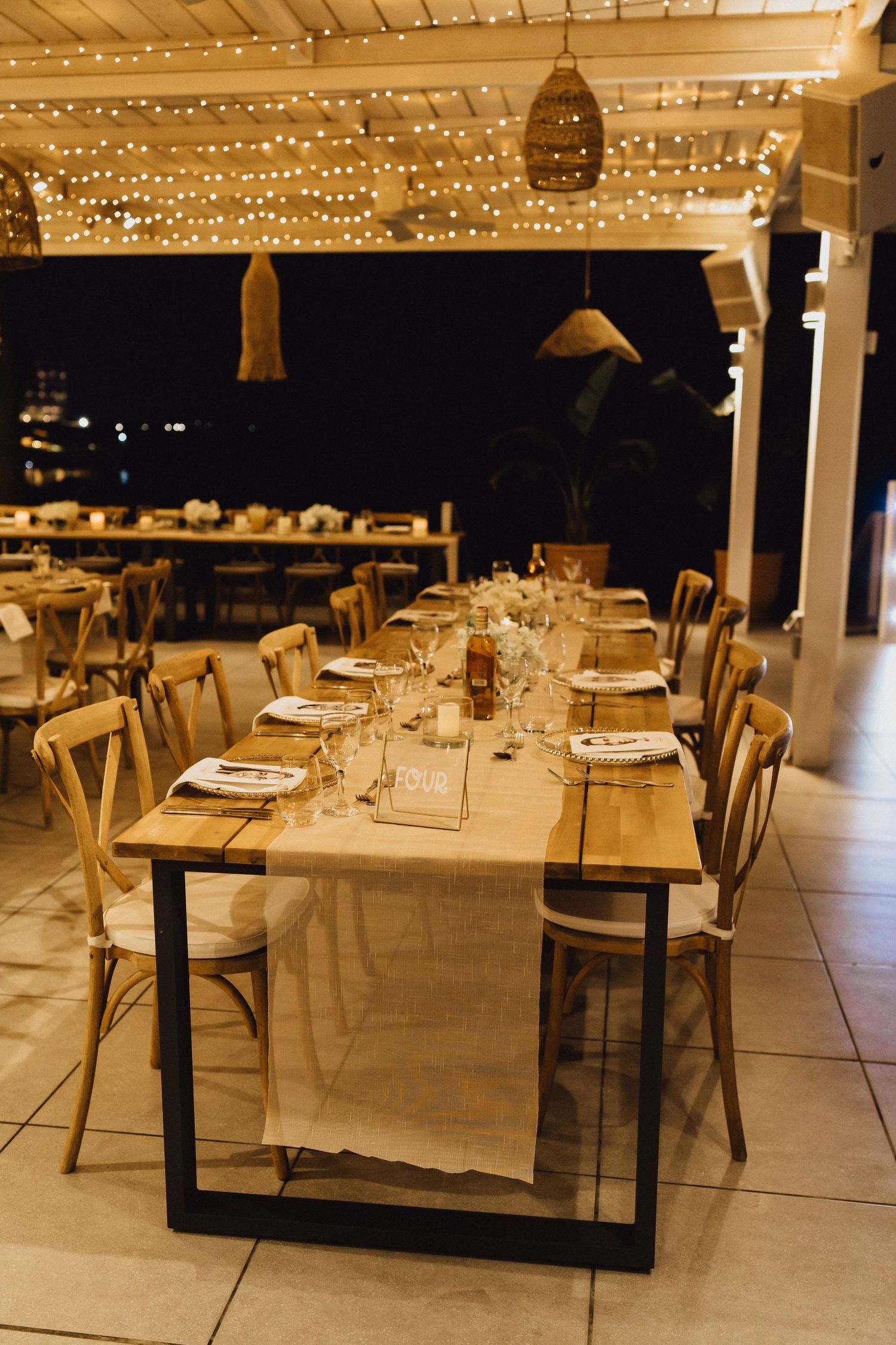 Elegant wedding reception table setting with string lights overhead and wooden chairs at a modern venue.